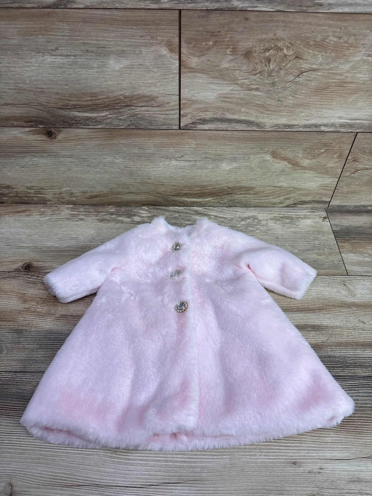 Front view of pink faux fur coat with three decorative buttons on a wood-look background