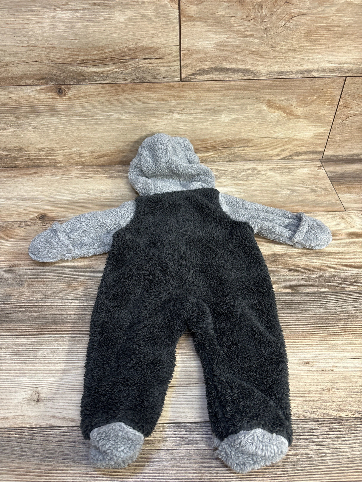 Plush black and gray baby onesie with hood on wooden floor