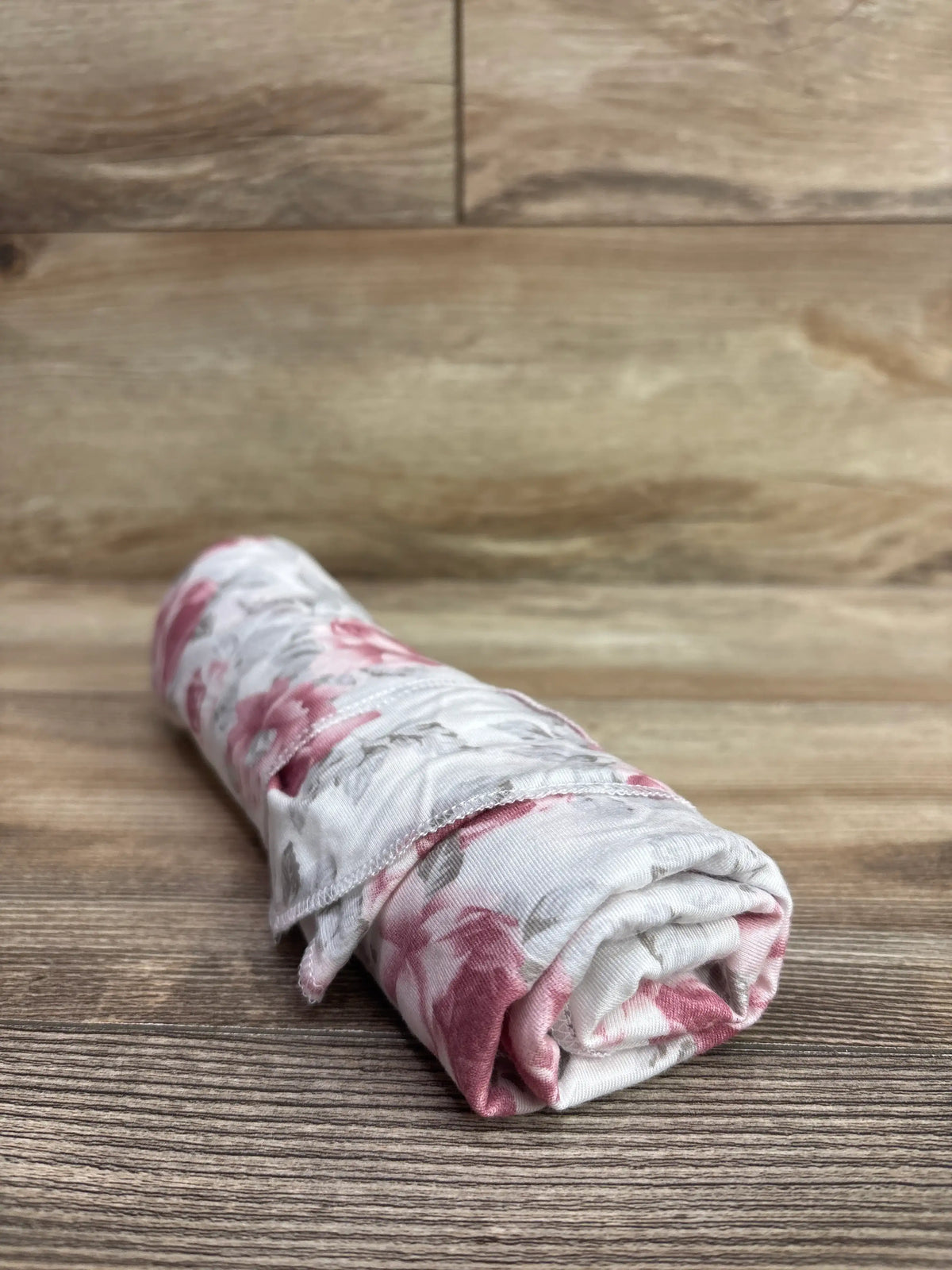 Rolled white viscose baby swaddle blanket with pink floral print on a wooden surface