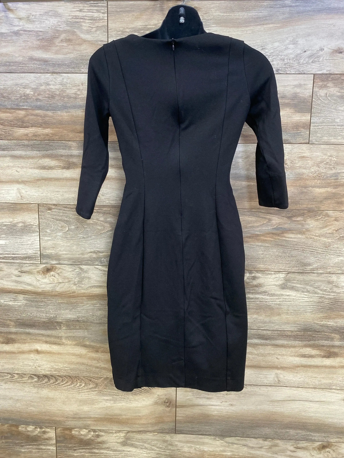 Front view of Seraphine black 3/4 sleeve maternity dress on hanger showing fitted silhouette, mock neck and back zipper on wood background
