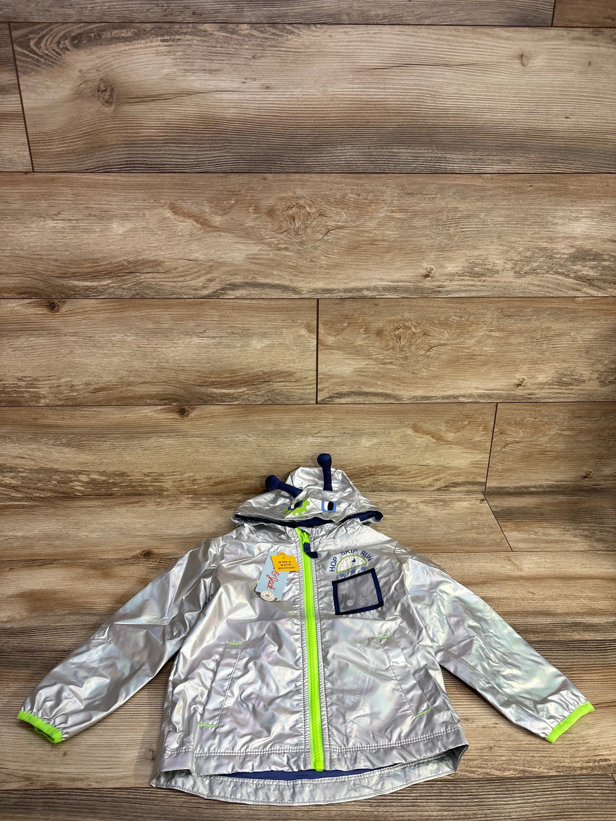 Silver reflective kids' hooded jacket with neon green zipper and playful hood antennae on wood floor