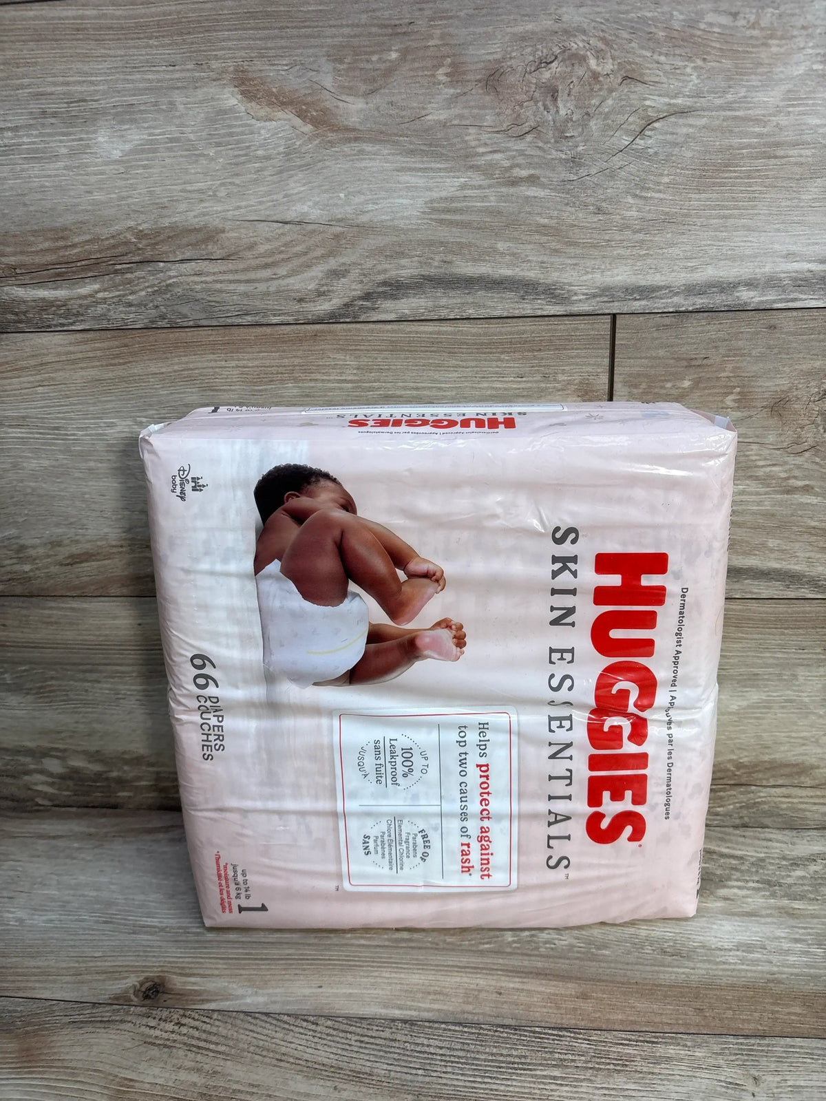 Front view of Huggies Skin Essentials size 1 diaper pack showing baby photo and 66 count label on light wood background