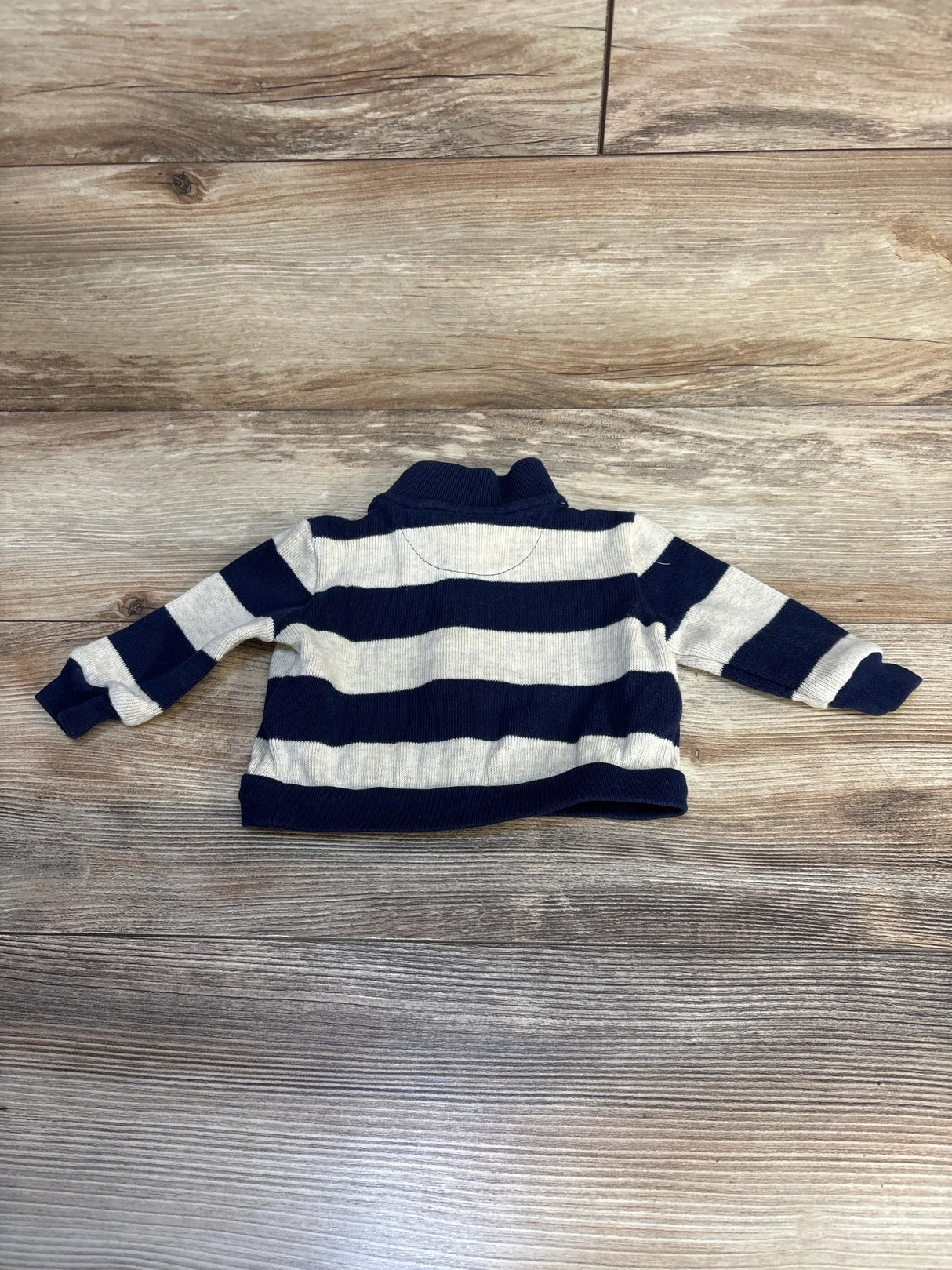 Navy and white striped long sleeve baby sweater on wooden floor