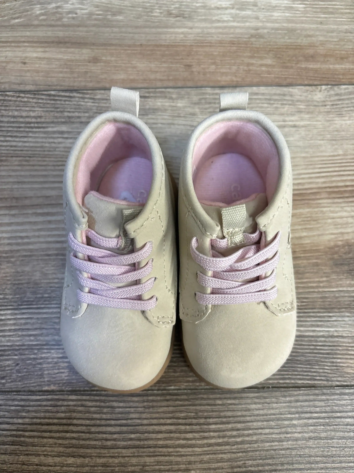 Top-down view of Just One You Cressida tan first-walker boots size 4C showcasing pink laces and pink lining on wood floor