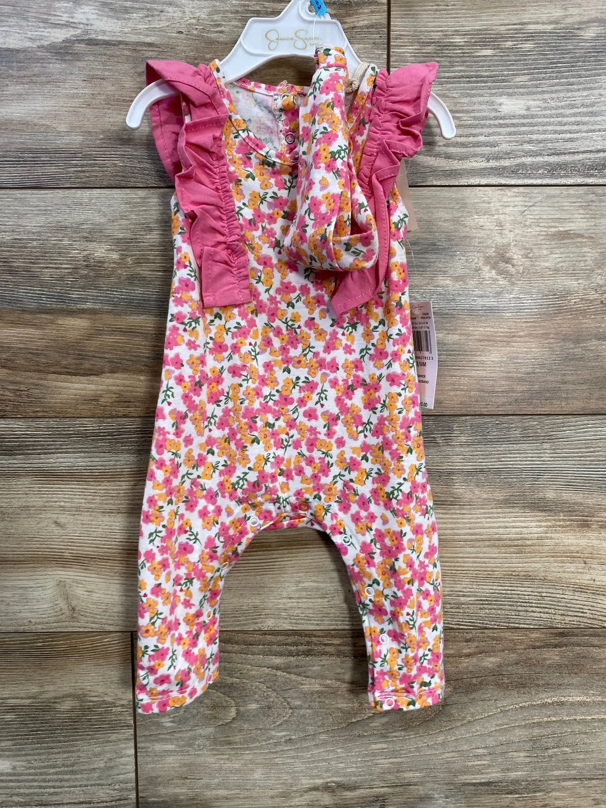 Front view of Jessica Simpson romper and matching headband, pink and orange floral print, ruffles and leg snaps on wood background