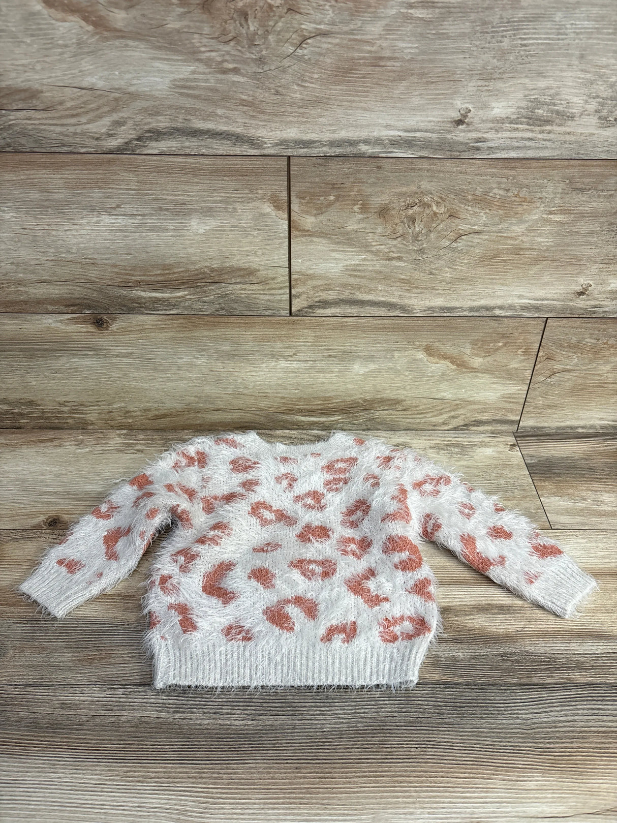 Flat lay of Jessica Simpson toddler fuzzy leopard-print sweatshirt, ivory with pink spots, fuzzy texture and ribbed hem on wooden floor