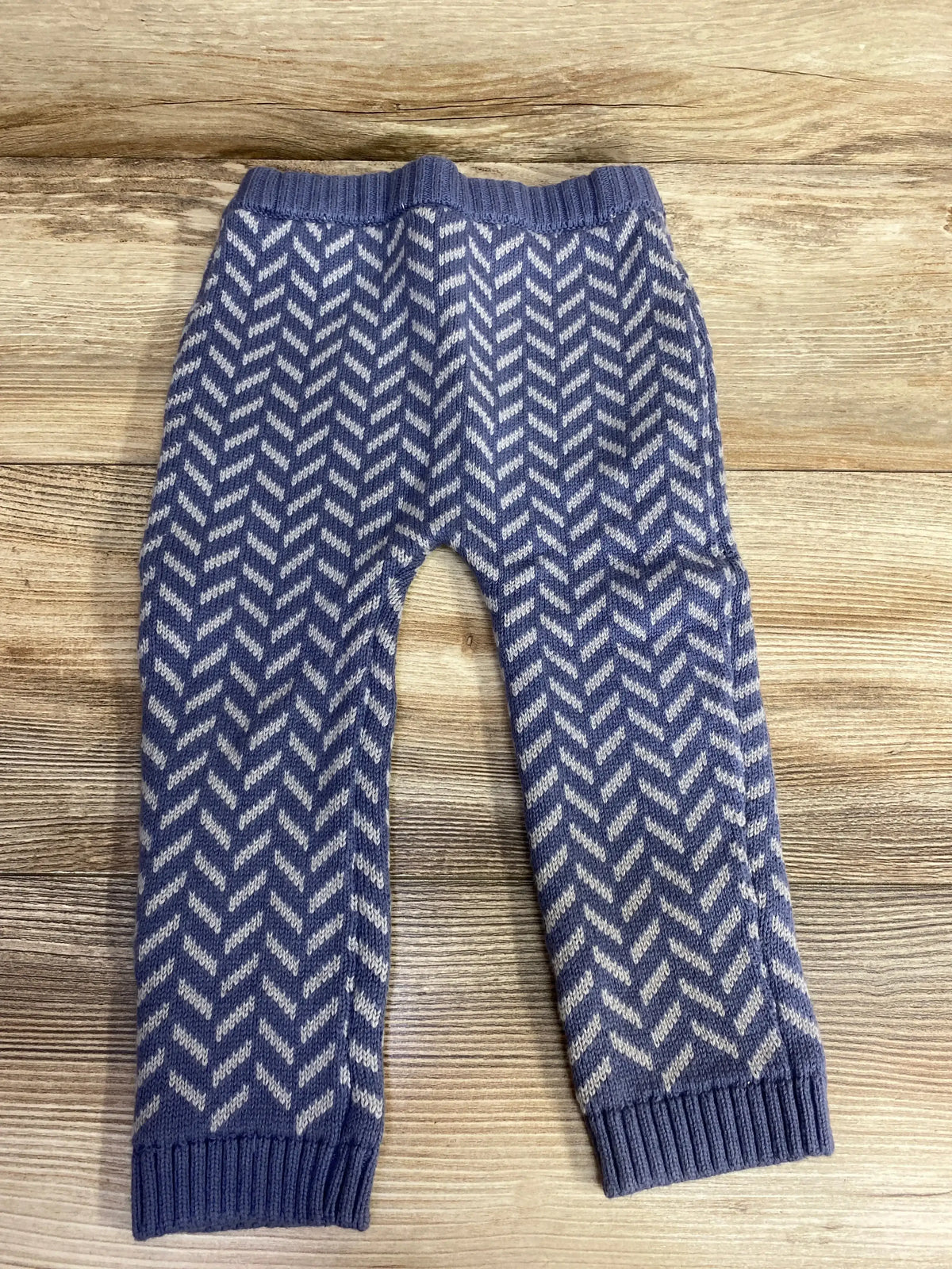 Blue and white knit baby pants with chevron pattern on wooden surface