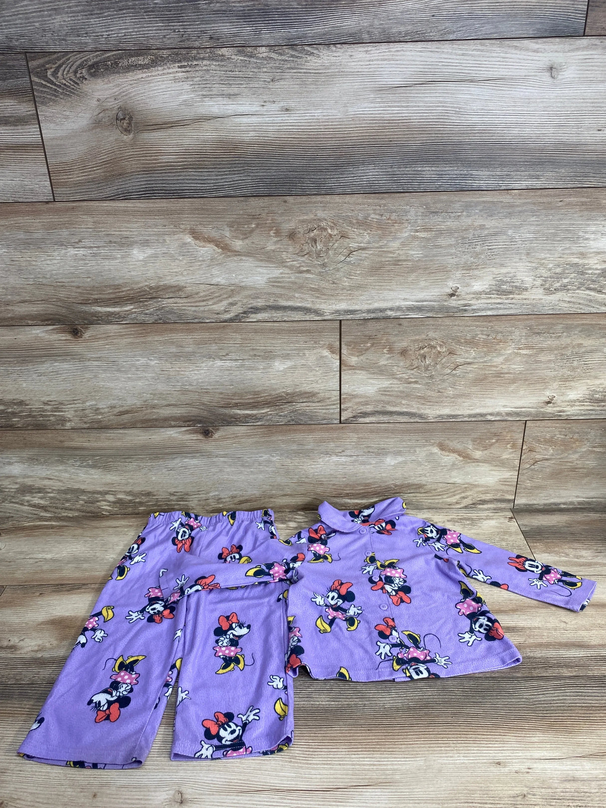 Purple toddler pajama set with Minnie Mouse print featuring pants and long-sleeve button-up top on wood floor