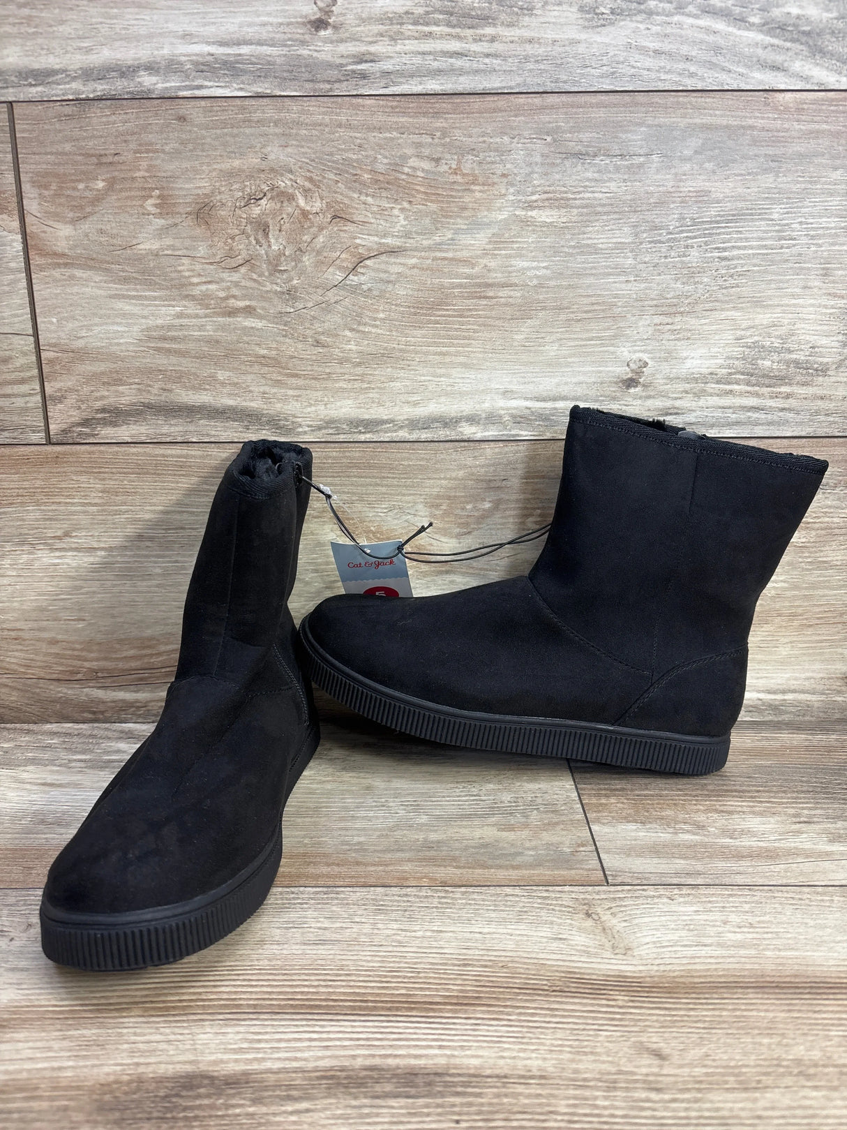 Black suede children’s ankle boots with rubber soles on wood floor background
