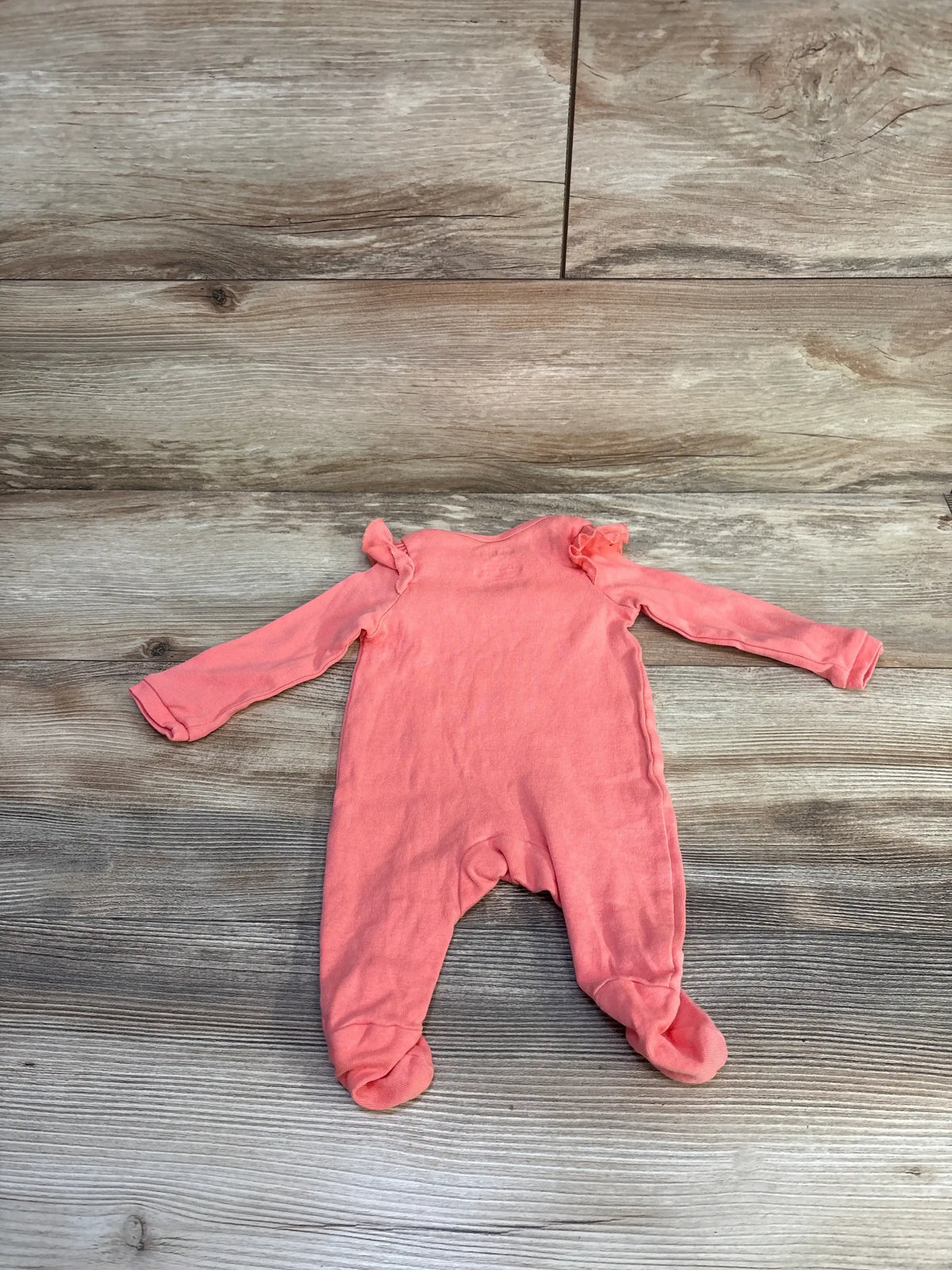 Front view of pink Okie Dokie footed coverall showcasing long sleeves and enclosed feet on a wood-look floor
