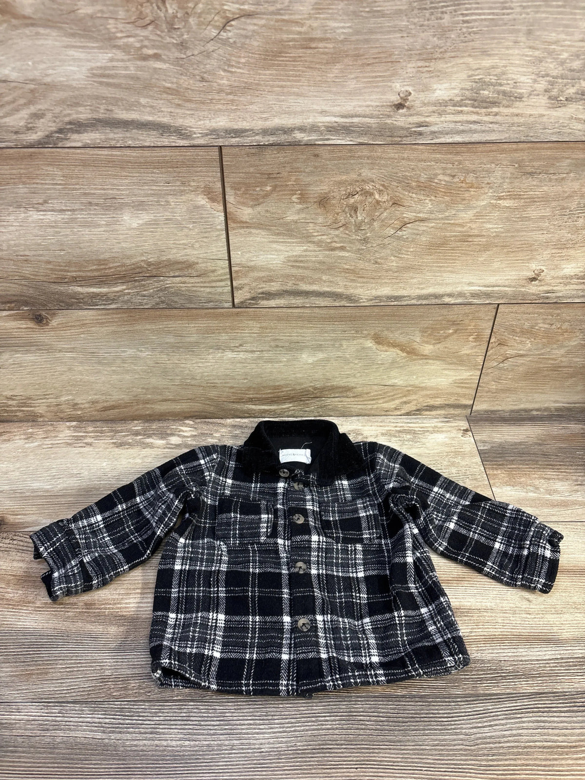 Top-down view of Scene & Heard black button-up shacket in size 12m, showcasing plaid pattern, collar, and buttons on wood floor