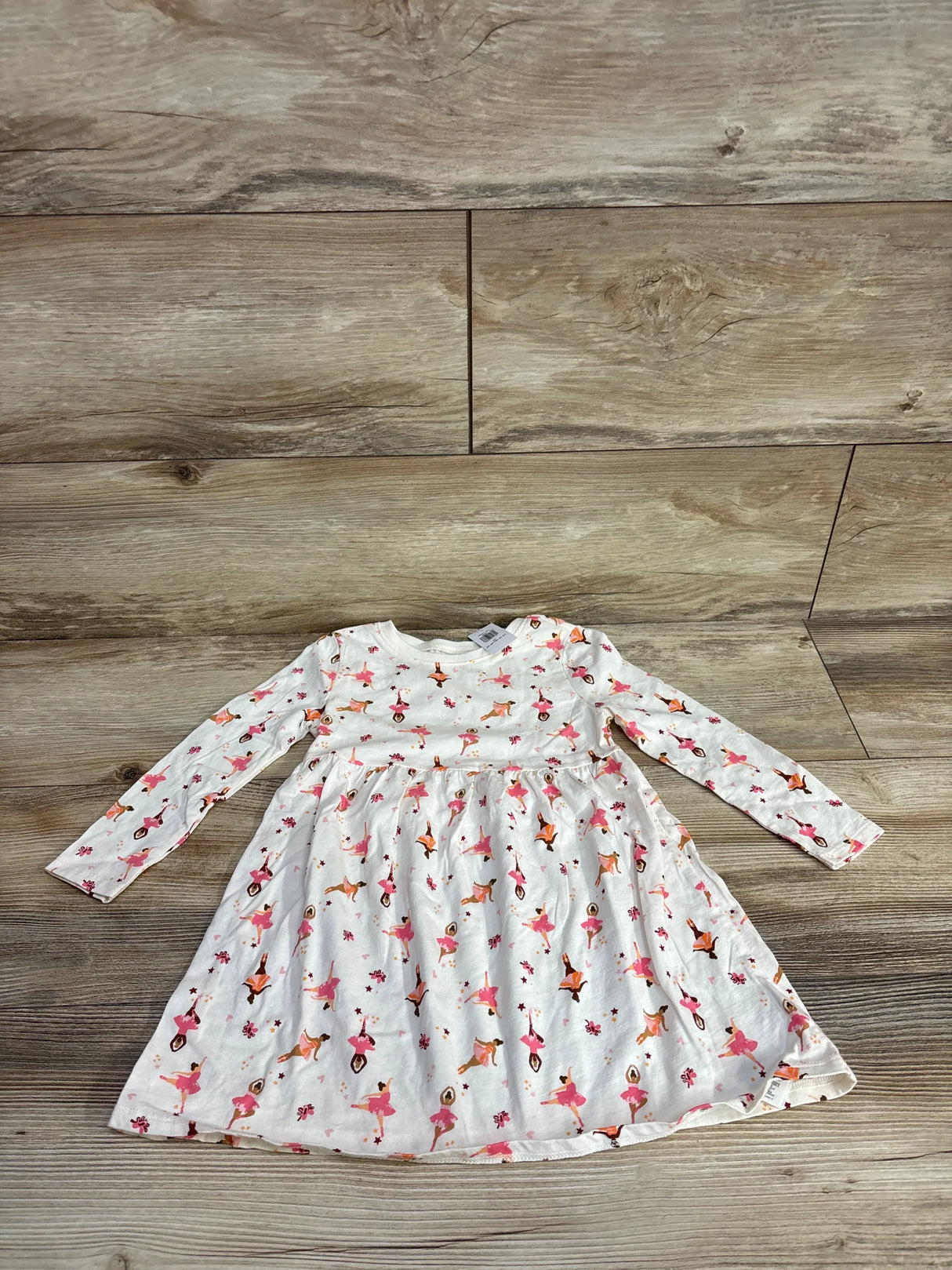 White long-sleeve toddler dress with pink and orange ballerina print on wooden floor background