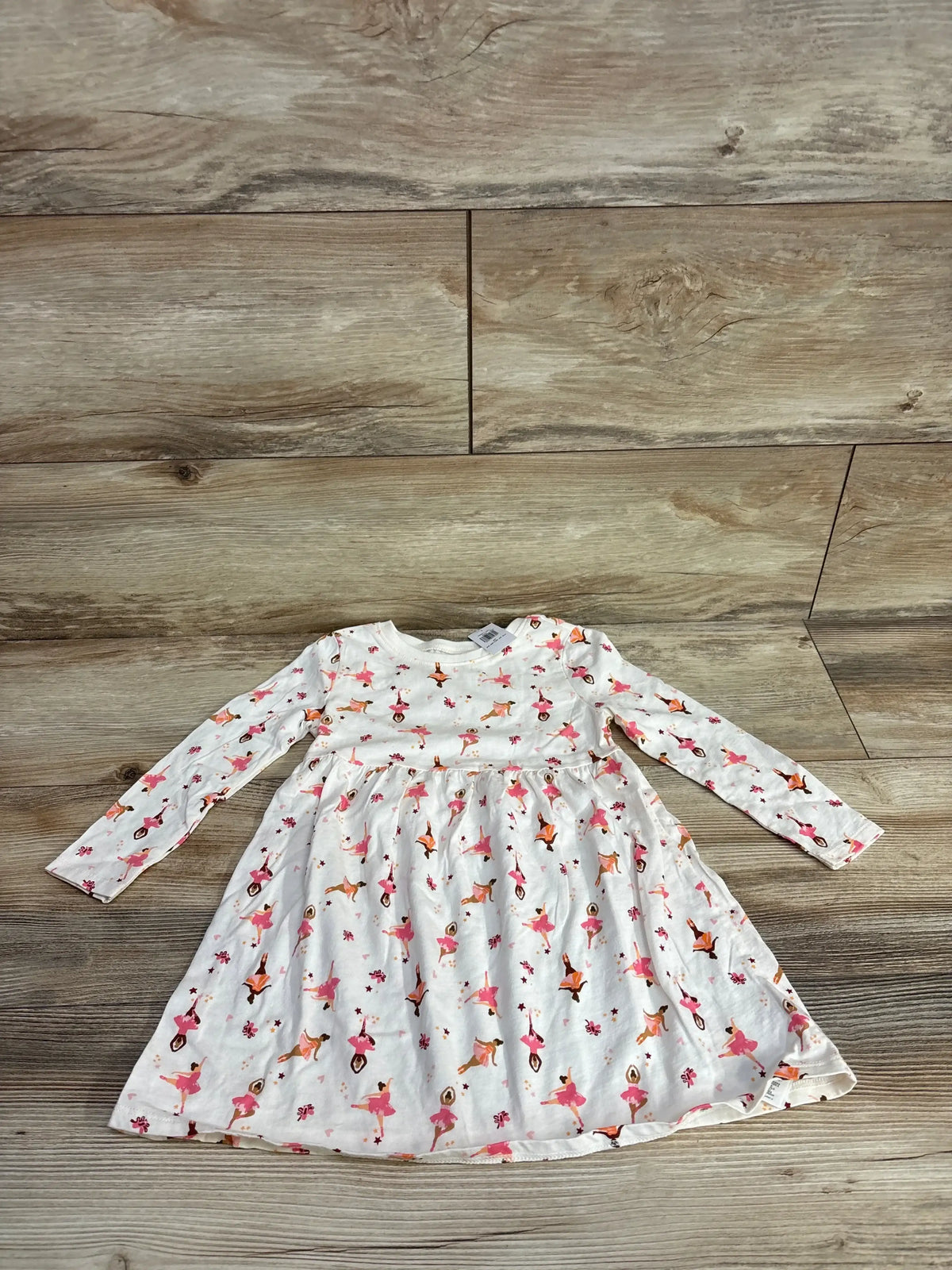 White long-sleeve toddler dress with pink and orange ballerina print on wooden floor background