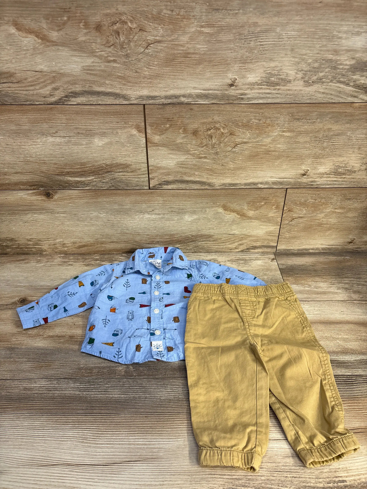 Top view of Baby B.U.M 12-month camping shirt and pants set with printed blue button-up shirt and tan pants on wood background