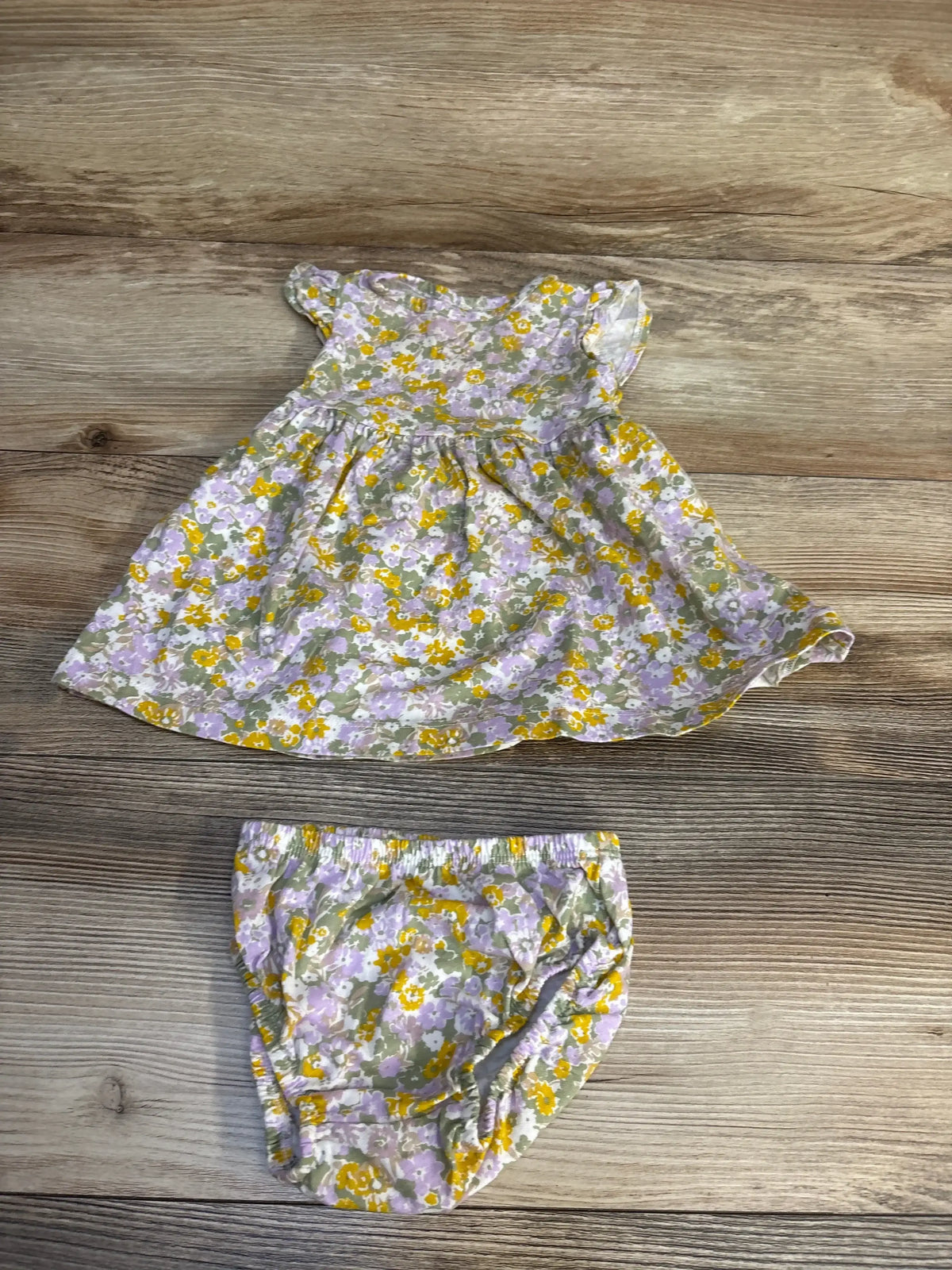 Floral baby dress and bloomers set with purple, yellow, and green print on wood background