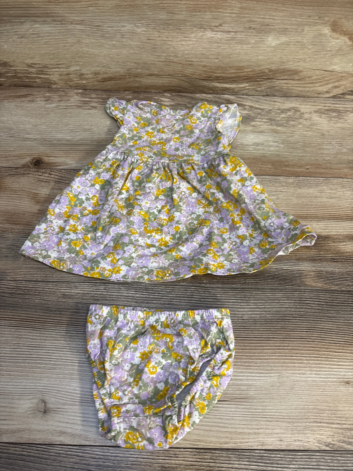 Floral baby dress and bloomers set with purple, yellow, and green print on wood background