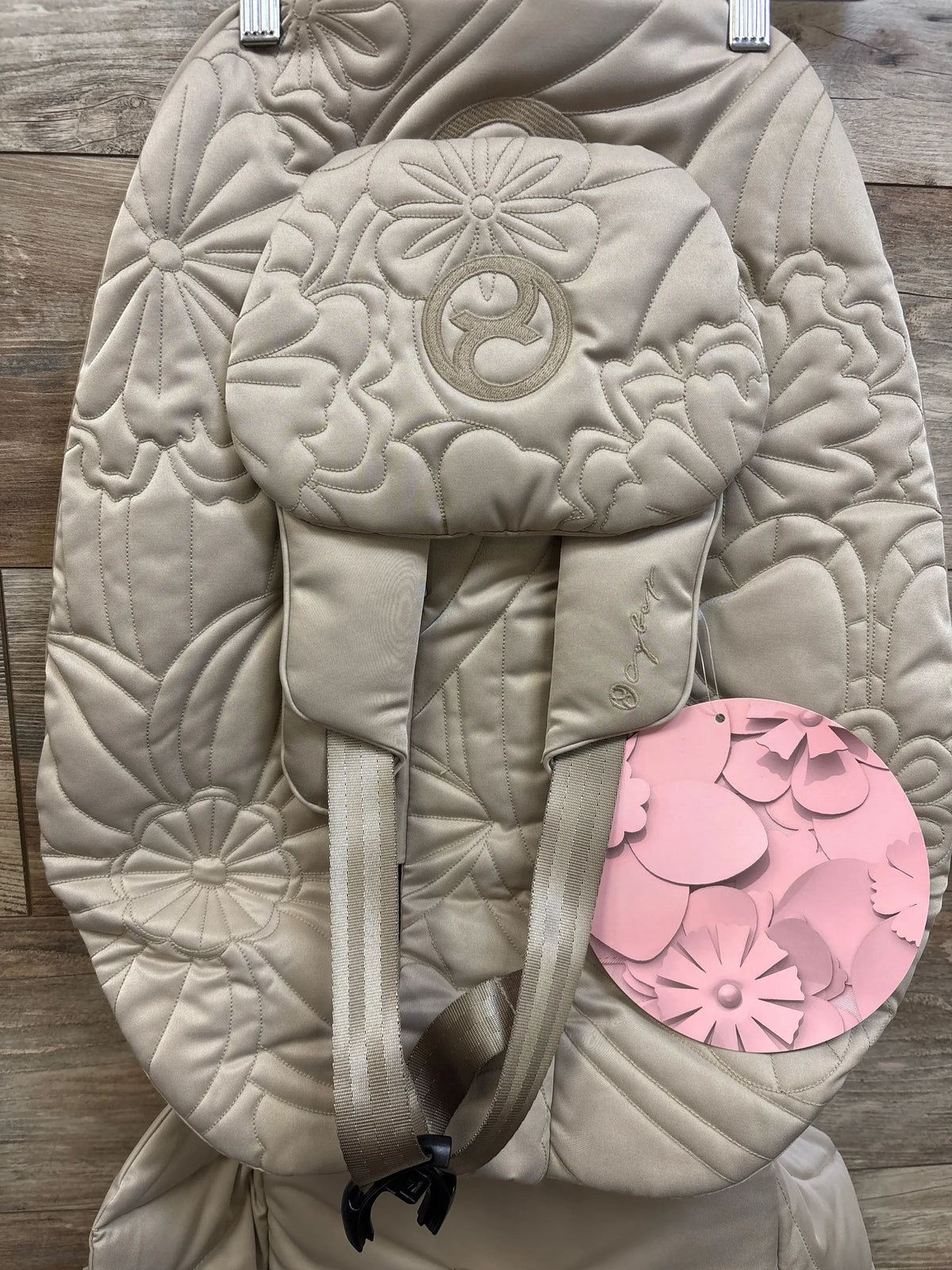Front view of Cybex Mios seat pack with padded floral quilting, embroidered headrest logo and harness straps on wood