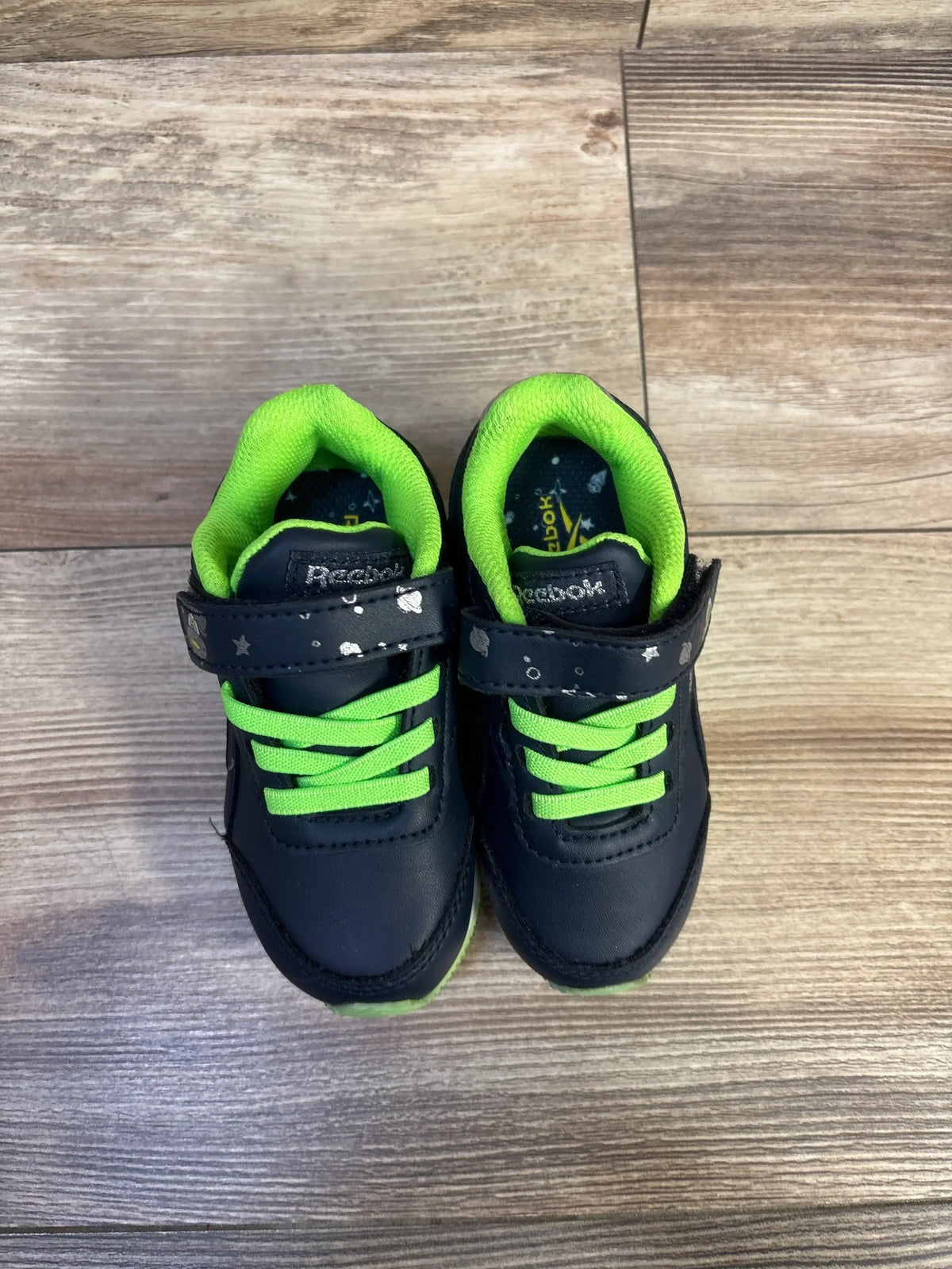 Top-front view of Reebok Space Sneakers in navy and green showcasing hook and loop closures on a wood floor