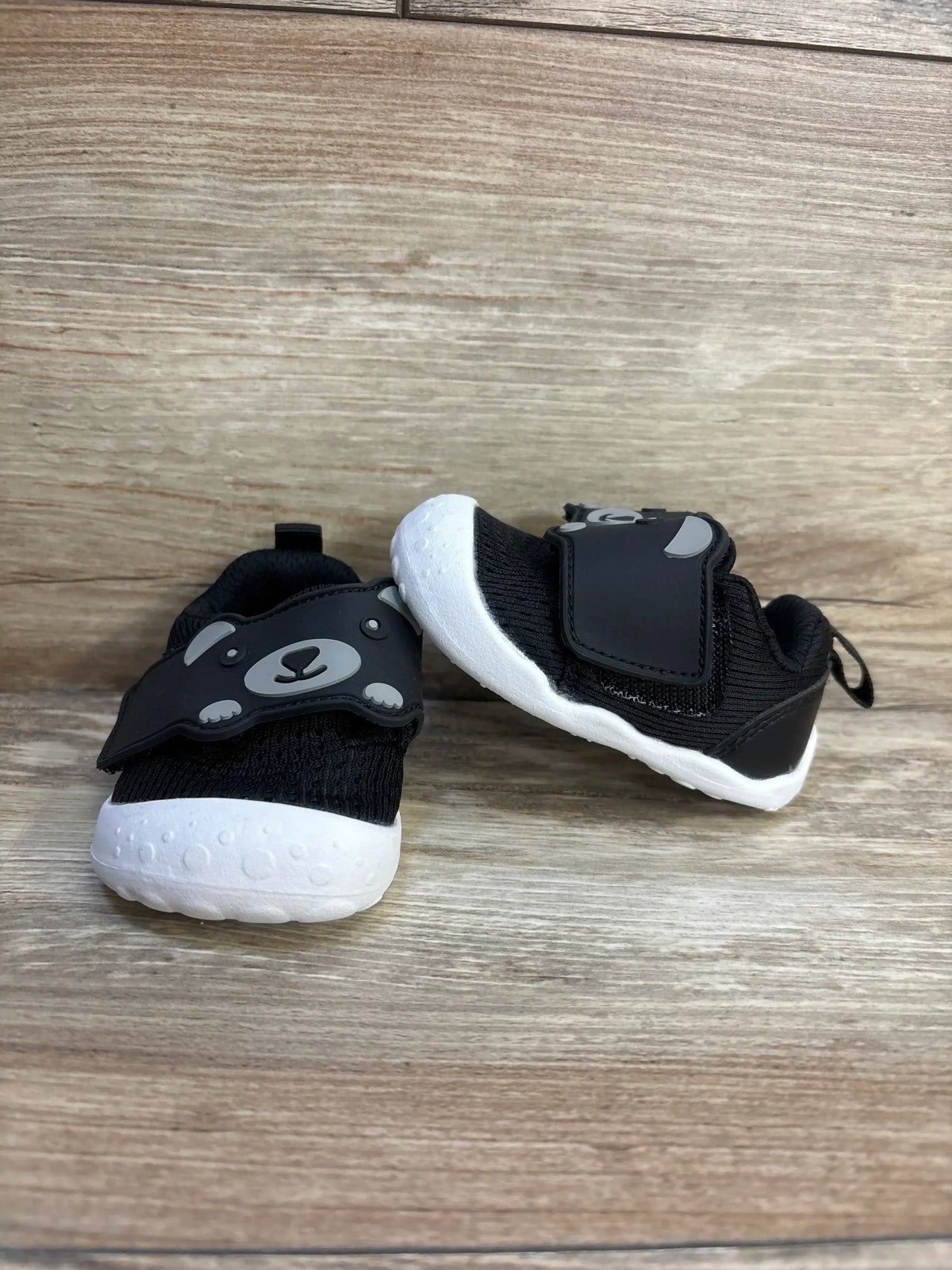 Three-quarter view of FEETCITY mesh toddler shoes with black knit upper, white soft sole, and bear-face velcro strap on wood backdrop
