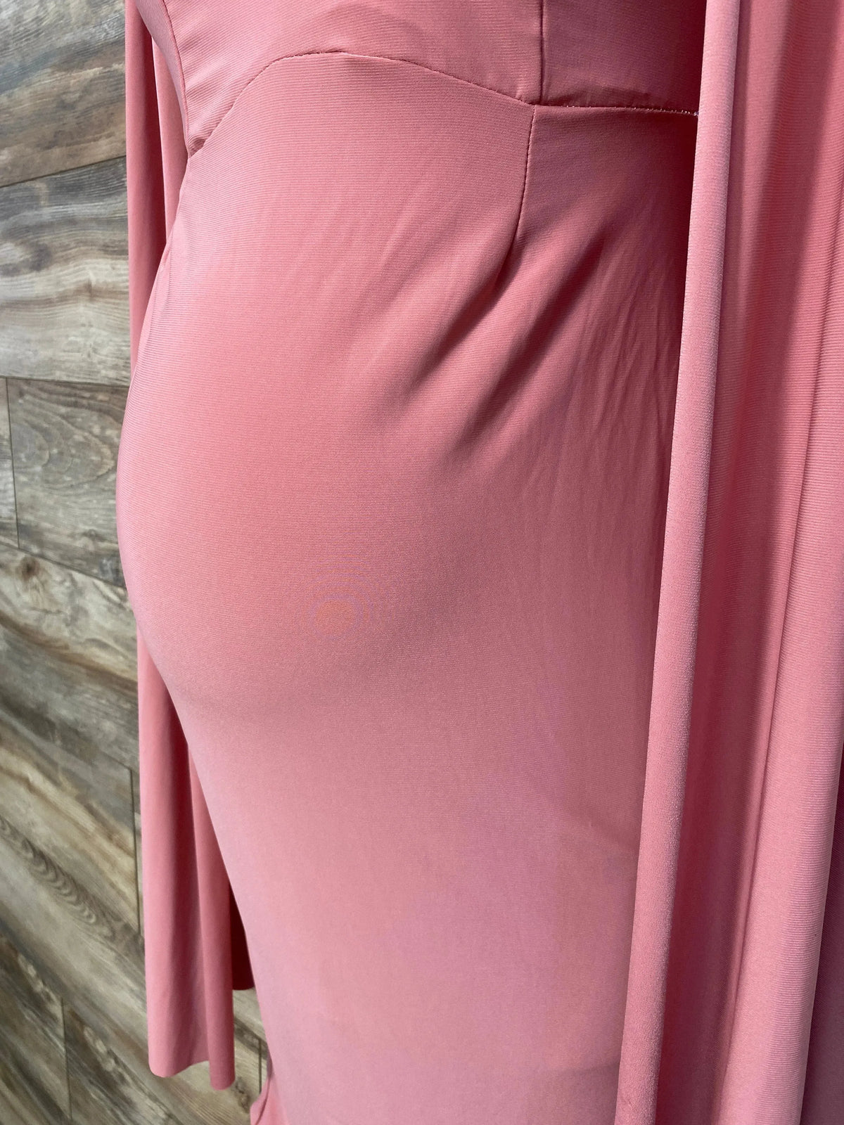 Side view of pink maternity dress showcasing fitted silhouette and cape sleeves with wood-plank background