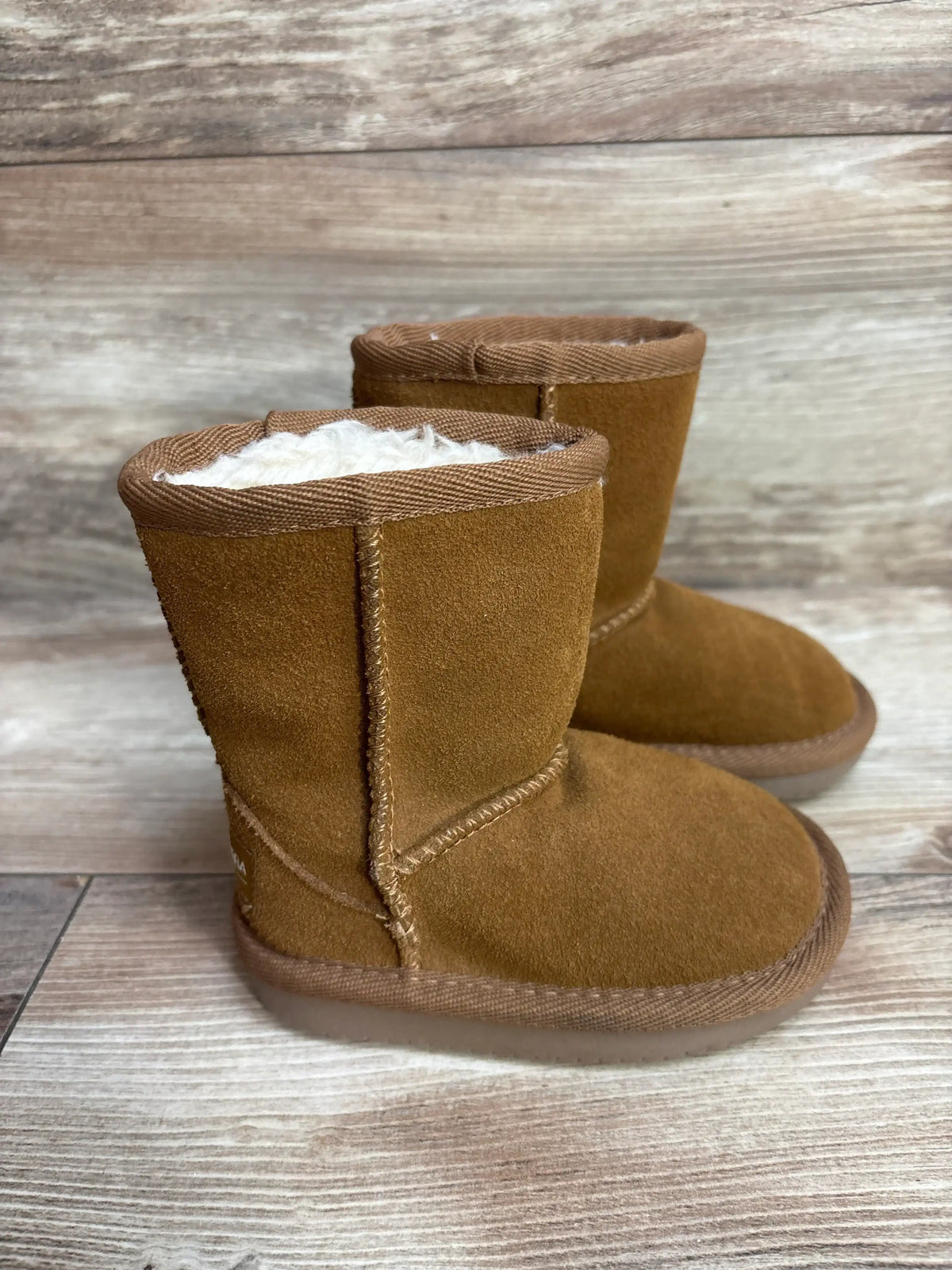 Side view of Koolaburra brown faux fur short toddler boots size 5C showing white faux fur lining and suede on wood floor