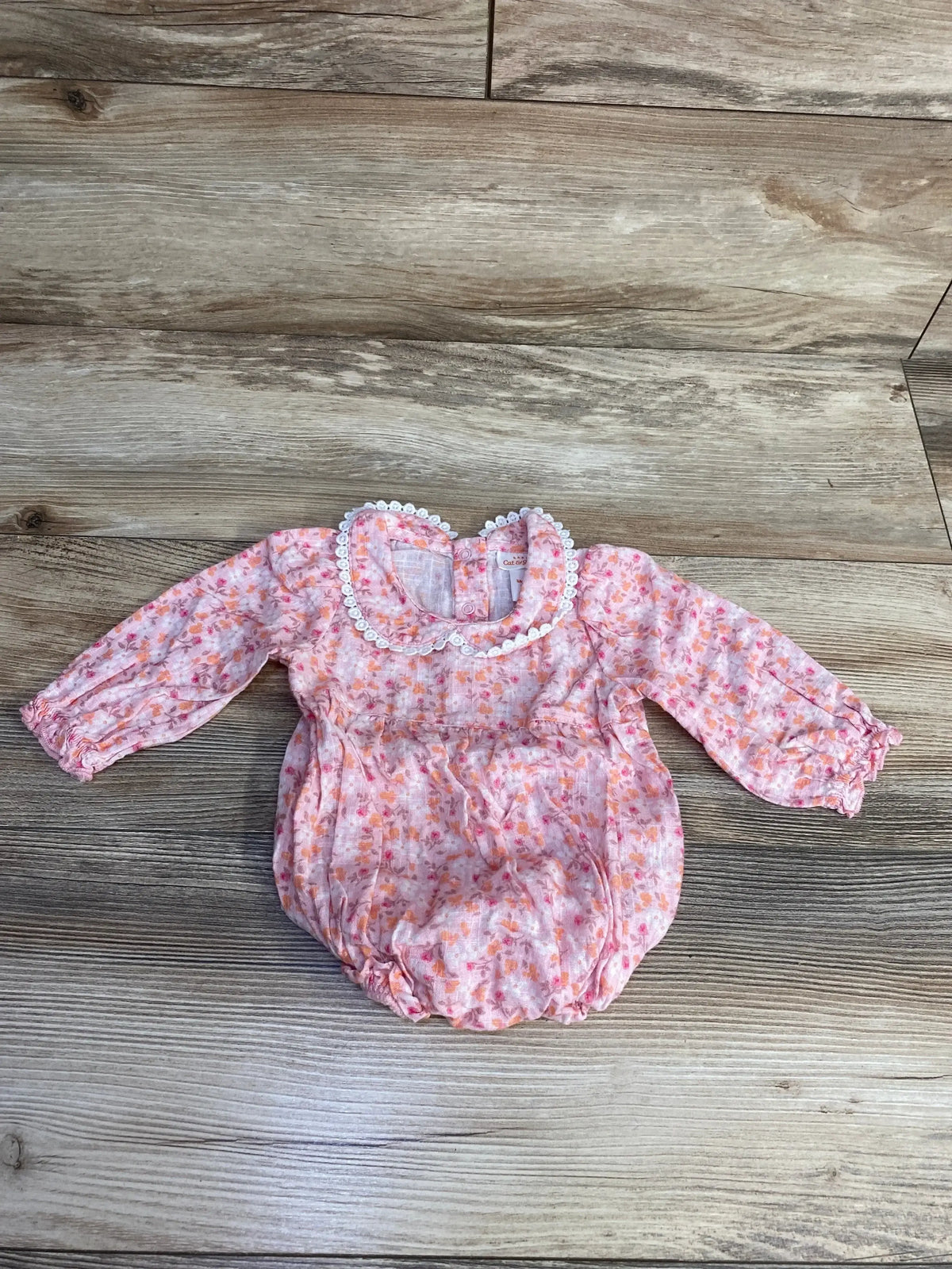 Flat lay of pink Cat & Jack long-sleeve floral baby romper showing lace-trimmed Peter Pan collar, gathered waist, and elastic leg openings on light wood background