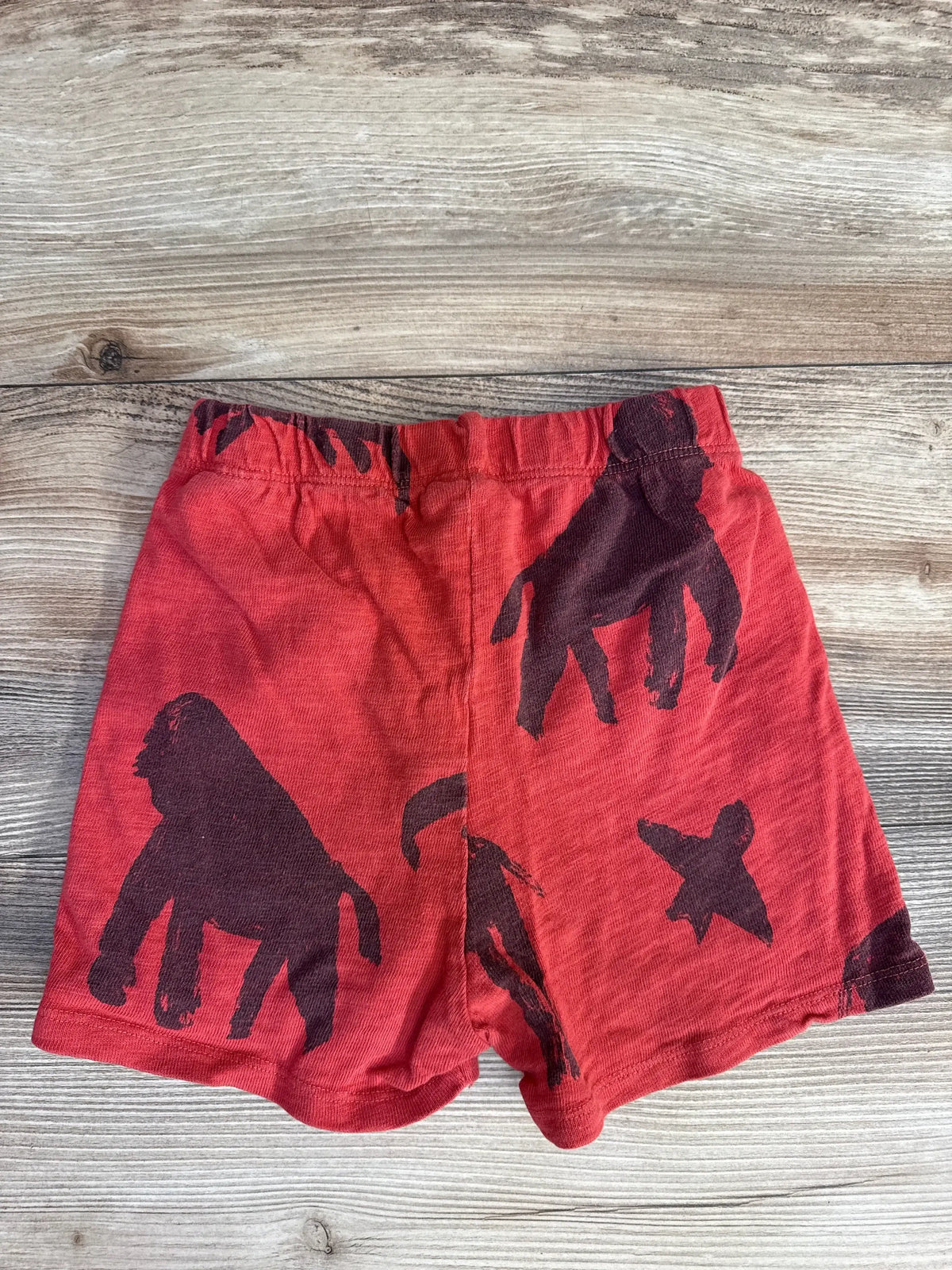 Front view of red Zara toddler shorts showcasing dark brown animal and hand silhouettes and elastic waistband on light wood background