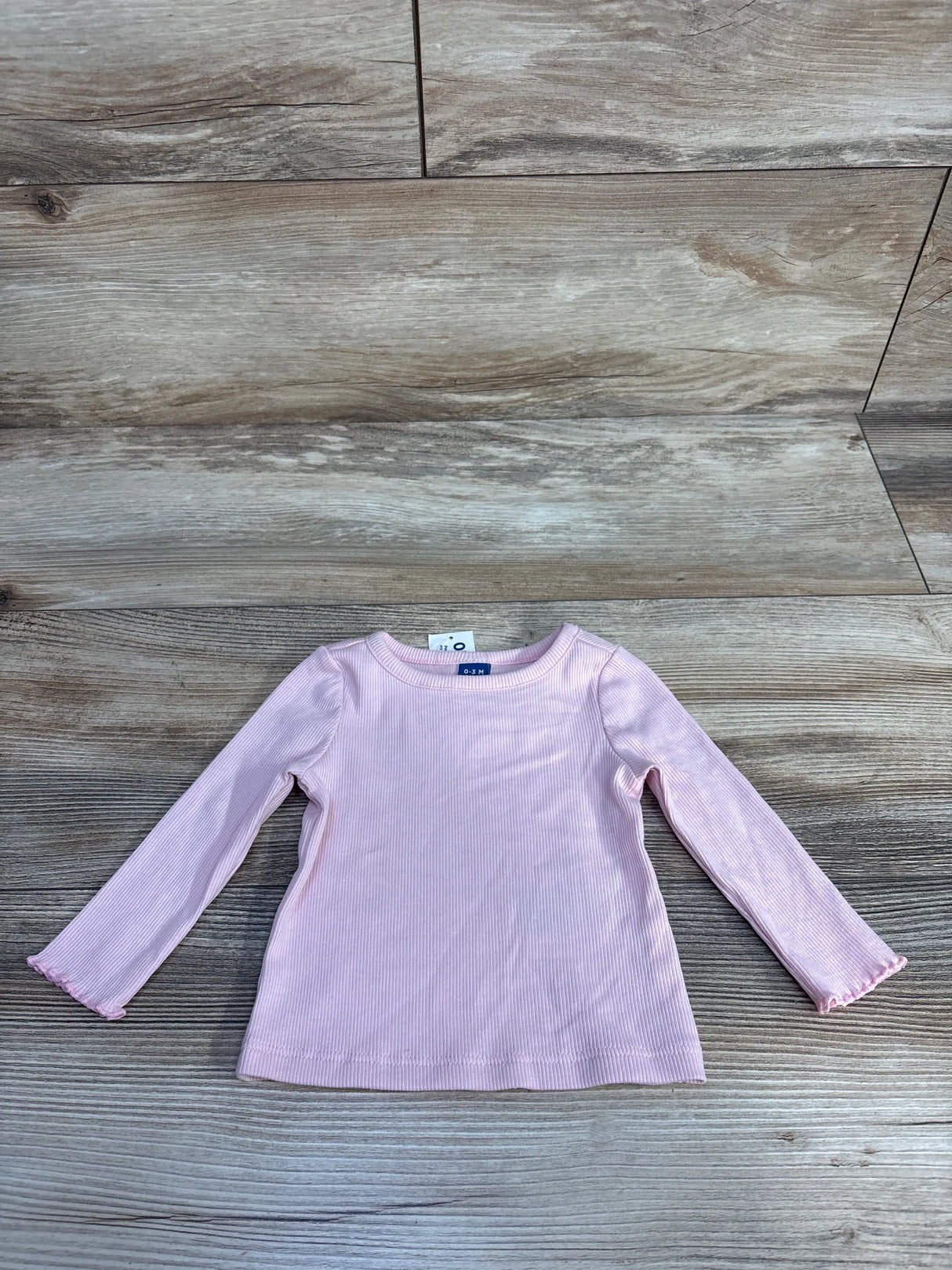 Pink long-sleeve ribbed baby shirt size 0-3 months on wooden floor background