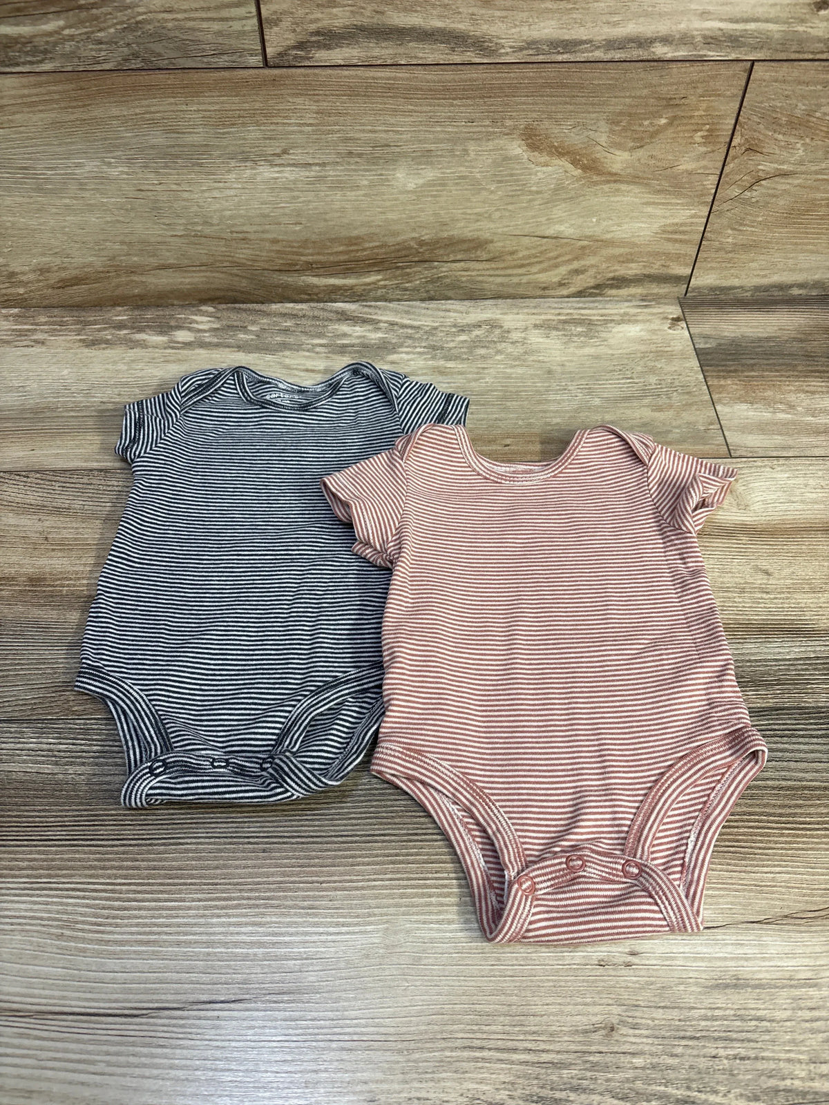Front view of Carter’s 2pk striped short-sleeve bodysuits in black and pink on a wood floor