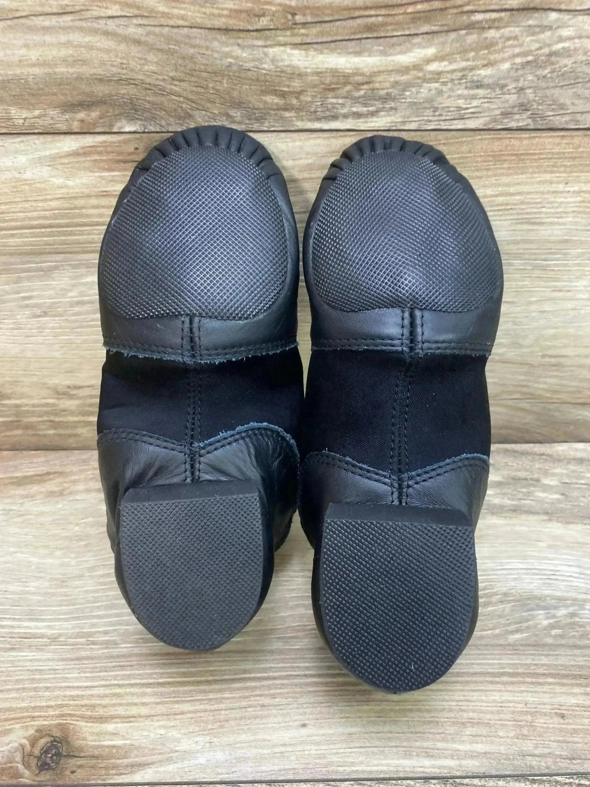 Top down view of Capezio E-Series black jazz shoes showcasing textured toe caps and low heels on wood plank background