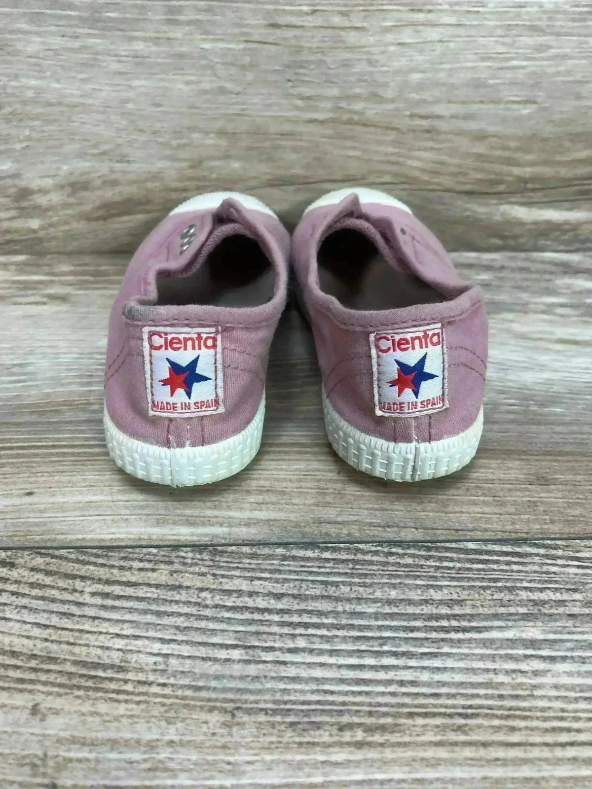 Rear view of pink distressed canvas slip-on sneakers showcasing no-lace elastic openings and sturdy rubber soles on a wood-grain surface
