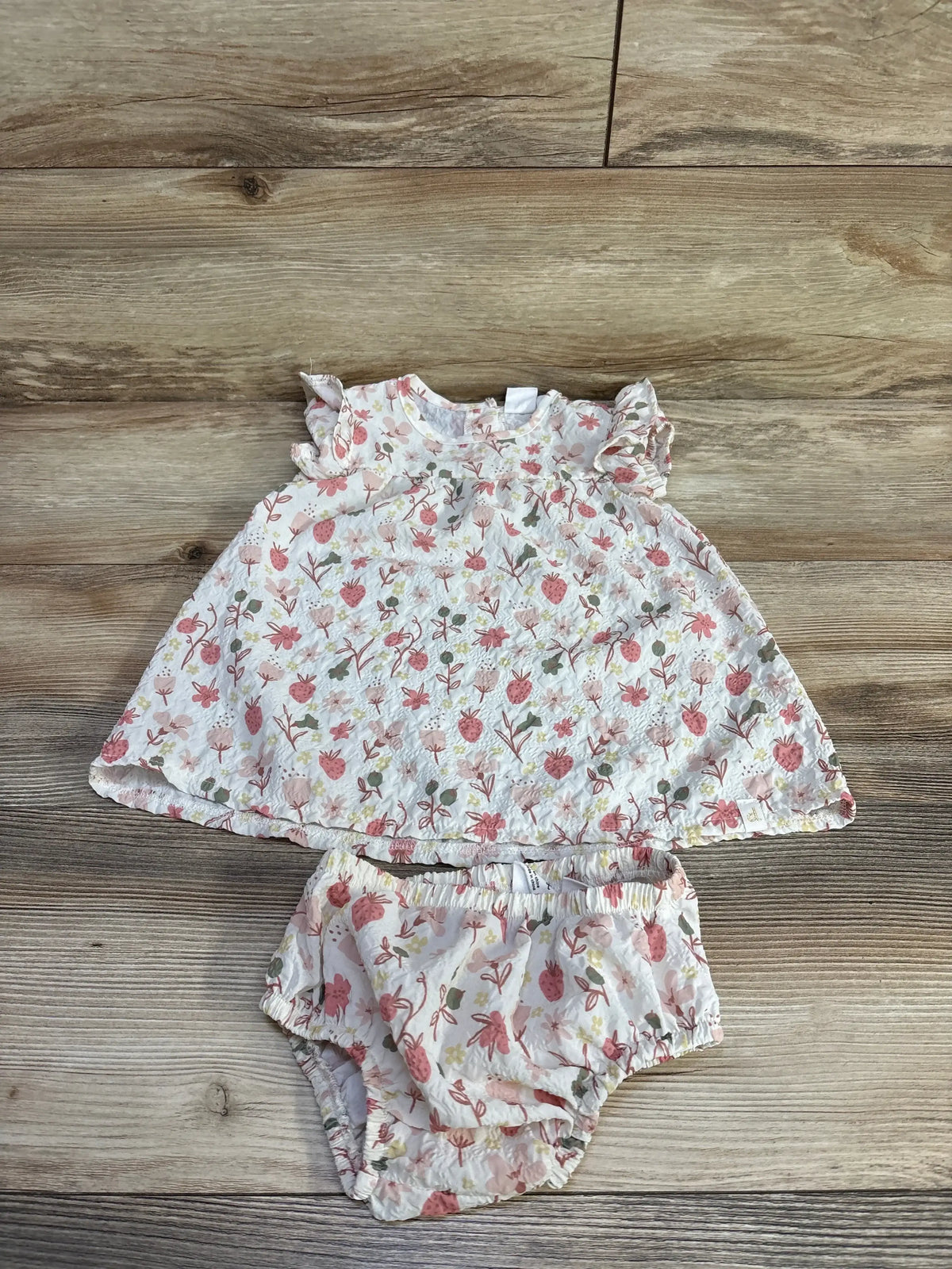 Front view of Deux Par Deux baby dress and bloomers set size 12m showcasing flower and strawberry print on wood background