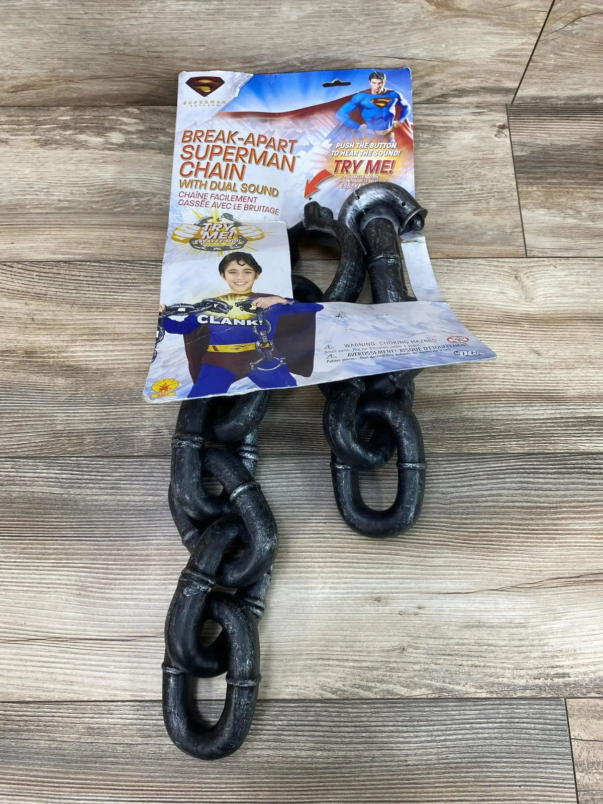Top view of Rubie’s break apart Superman chain showcasing black linked shackles, dual sound packaging, and wood floor