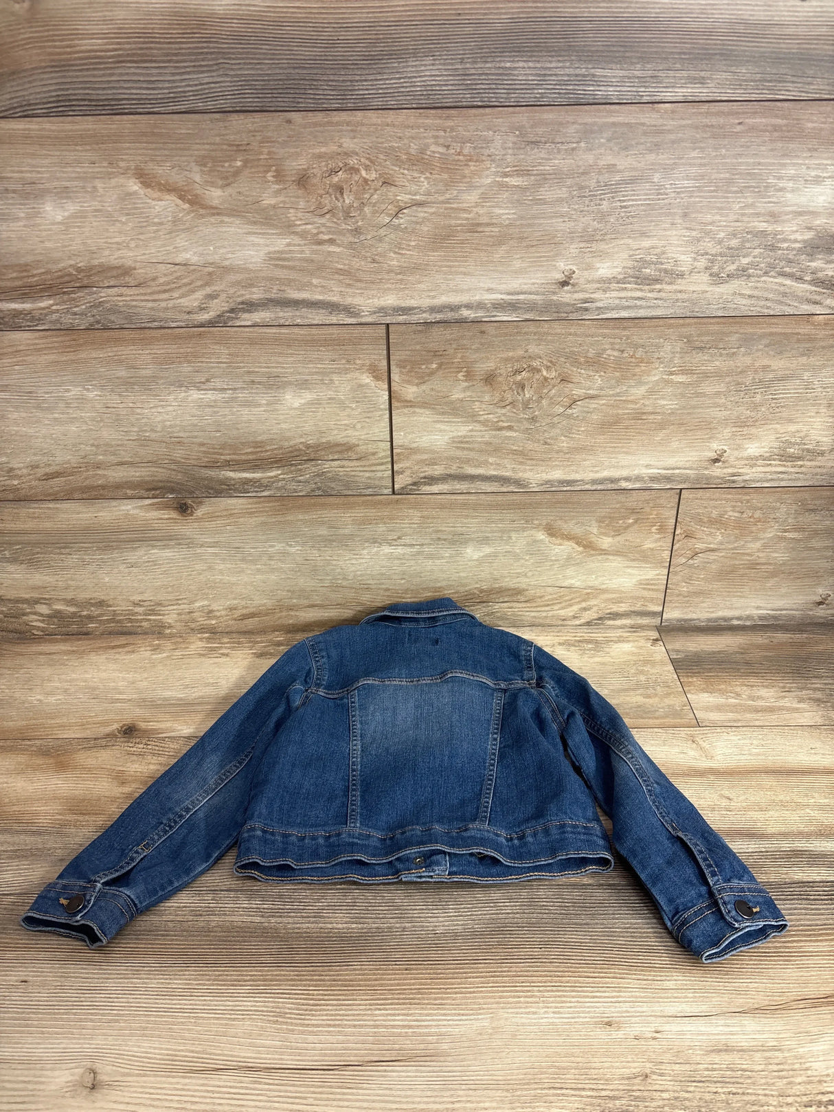 Back view of Children's Place denim jacket size 5T showing faded blue wash, button cuffs, and yoke stitching on wood plank background