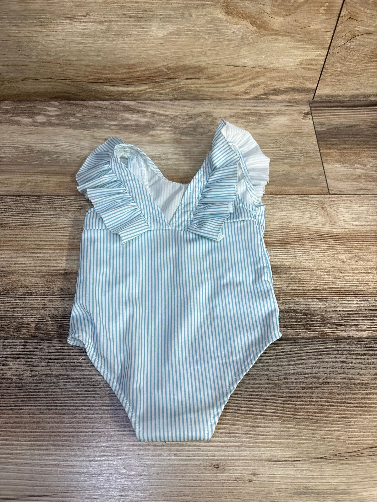 Front view of white striped ruffle one-piece swimsuit, size 2T, showcasing decorative ruffles on a wood floor
