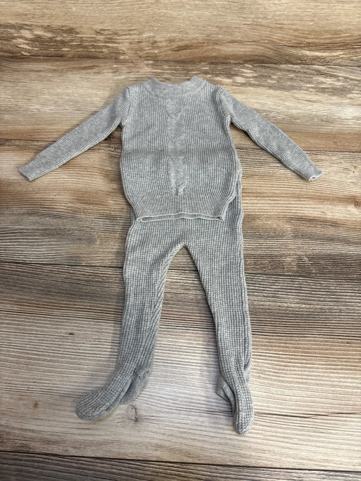 Flat lay of NooVel grey baby thermal shirt and footed pants showing ribbed knit and center cable detail on wood background