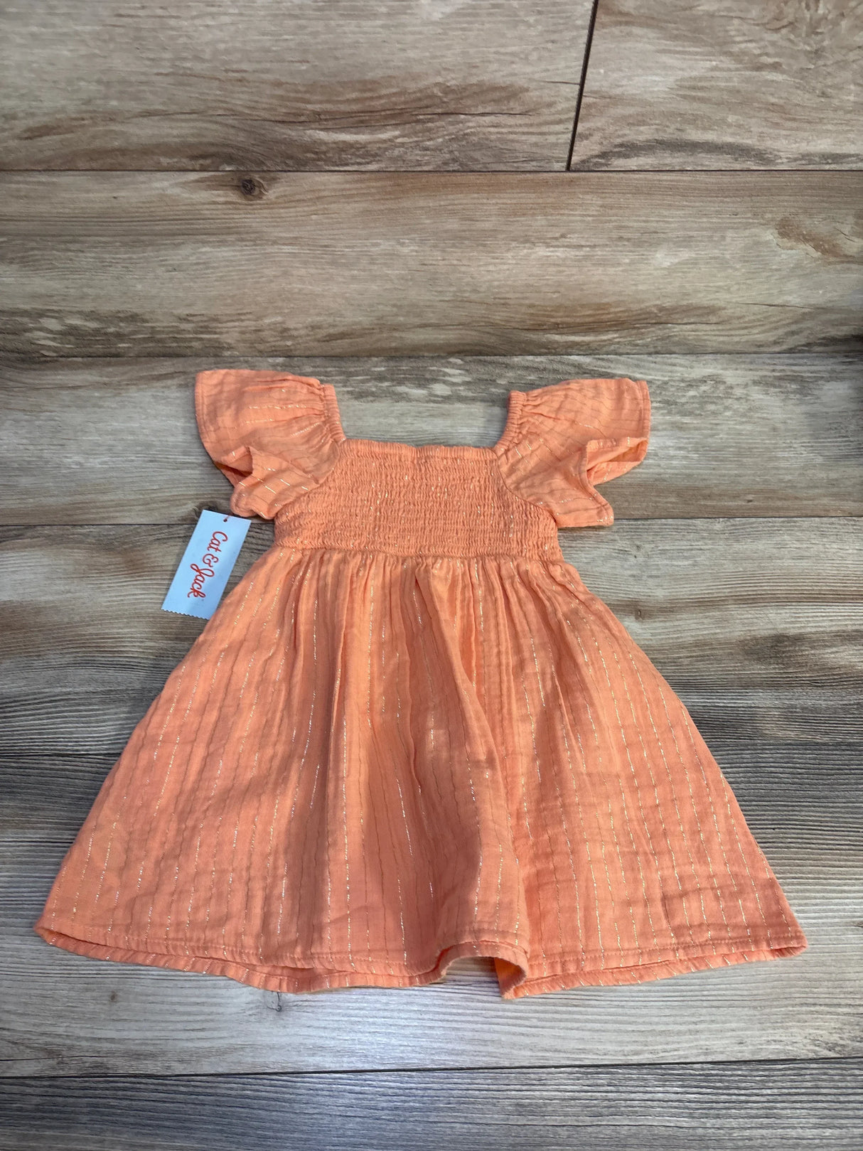 Peach baby dress with ruffle sleeves and shimmer stripes, Cat & Jack brand, laid on wood floor