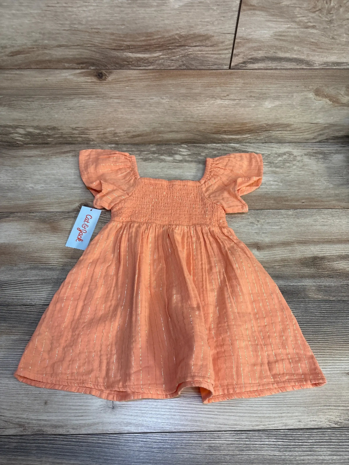 Peach baby dress with ruffle sleeves and shimmer stripes, Cat & Jack brand, laid on wood floor