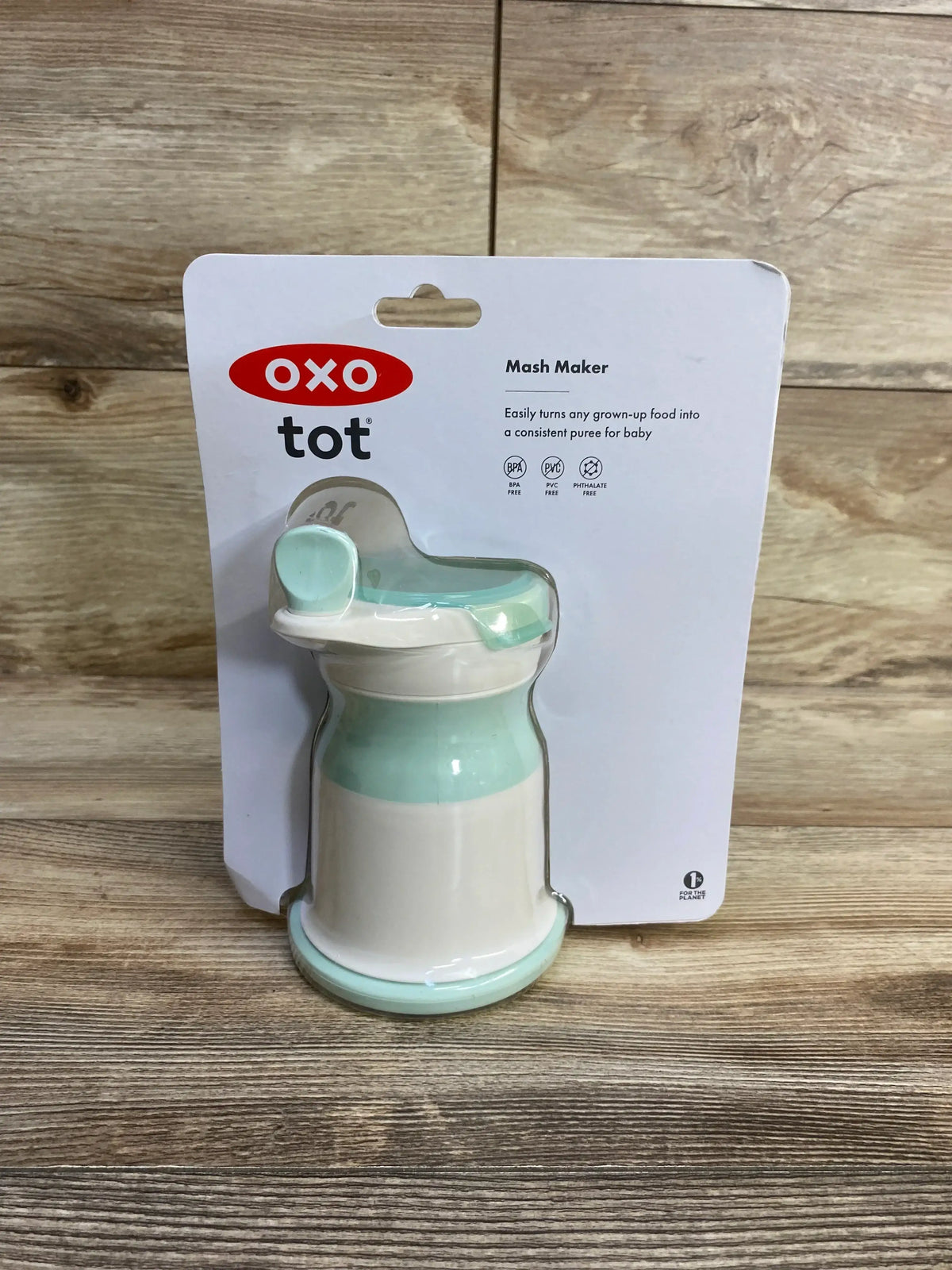 Front view of OXO Tot Mash Maker showcasing opal mint lid and mash mechanism on wood background