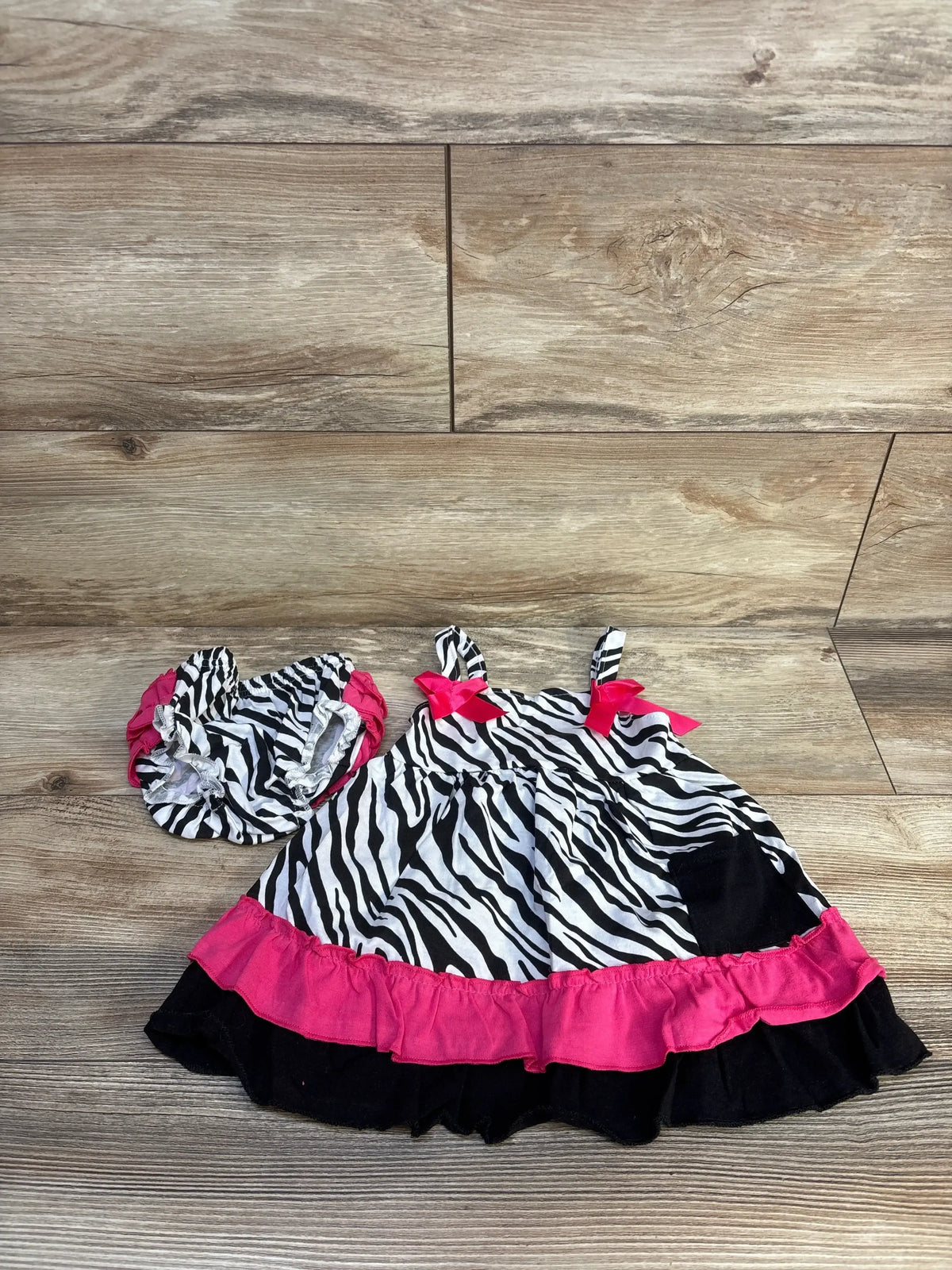 Flat lay of 2pc Zebra print top and bloomers set showcasing pink and black ruffle trim on wood floor