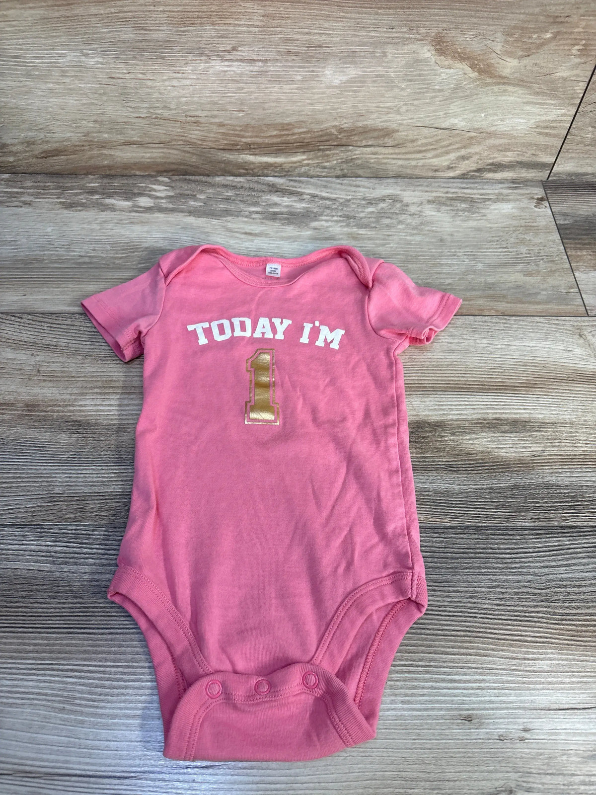 Front view of pink Okie Dokie 12-month bodysuit showcasing a Today I’m 1 birthday design on a wood-grain background