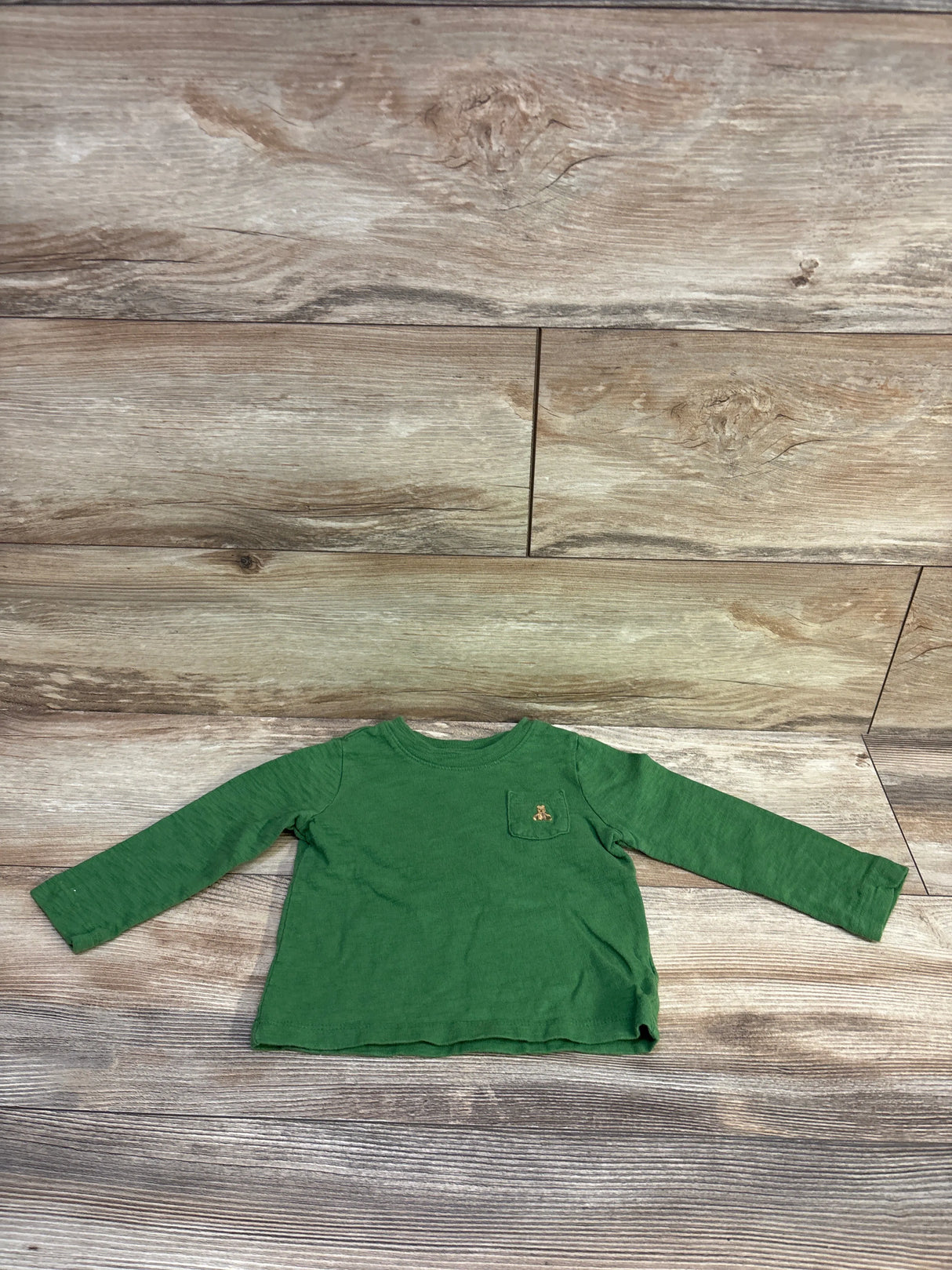 Flat lay of green Baby Gap long-sleeve pocket shirt (18-24 months) showing chest pocket with small embroidered bear on wood plank background