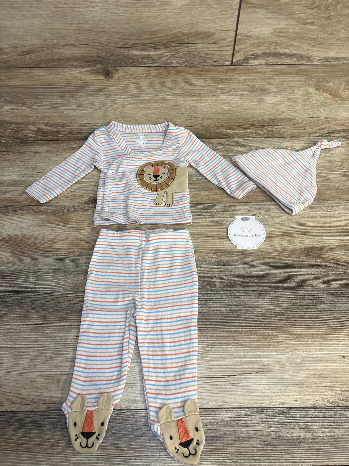 Striped baby clothes set with lion applique, pants with animal faces, and matching knotted hat on wooden floor