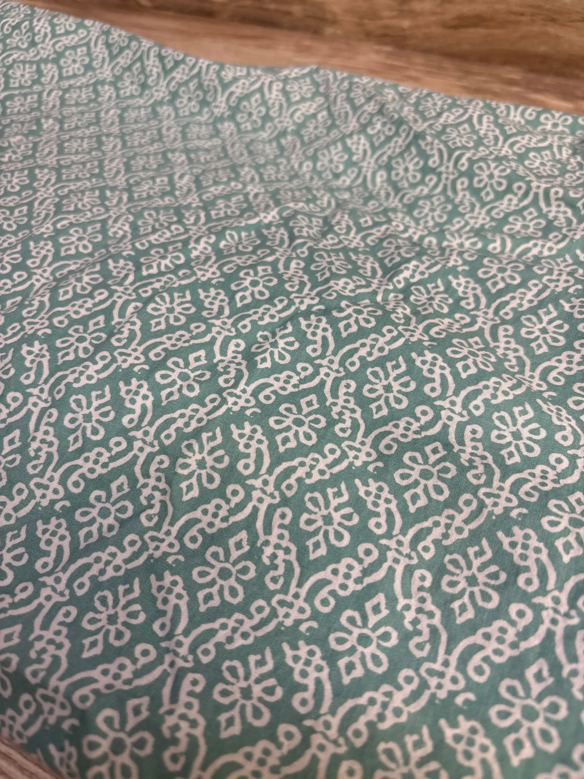 Close-up of Levtex Baby fitted crib sheet showcasing green fabric with white floral pattern on a wood background