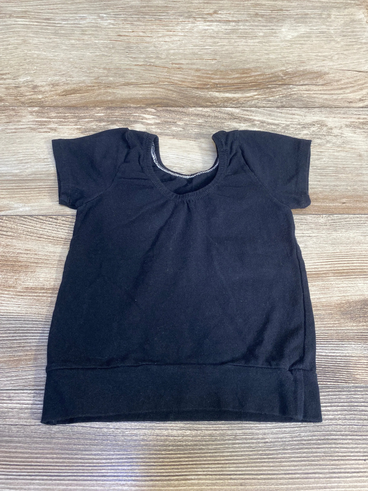 Flat lay of black short-sleeve toddler shirt size 12-18 months showing scoop neckline and banded hem on light wood background