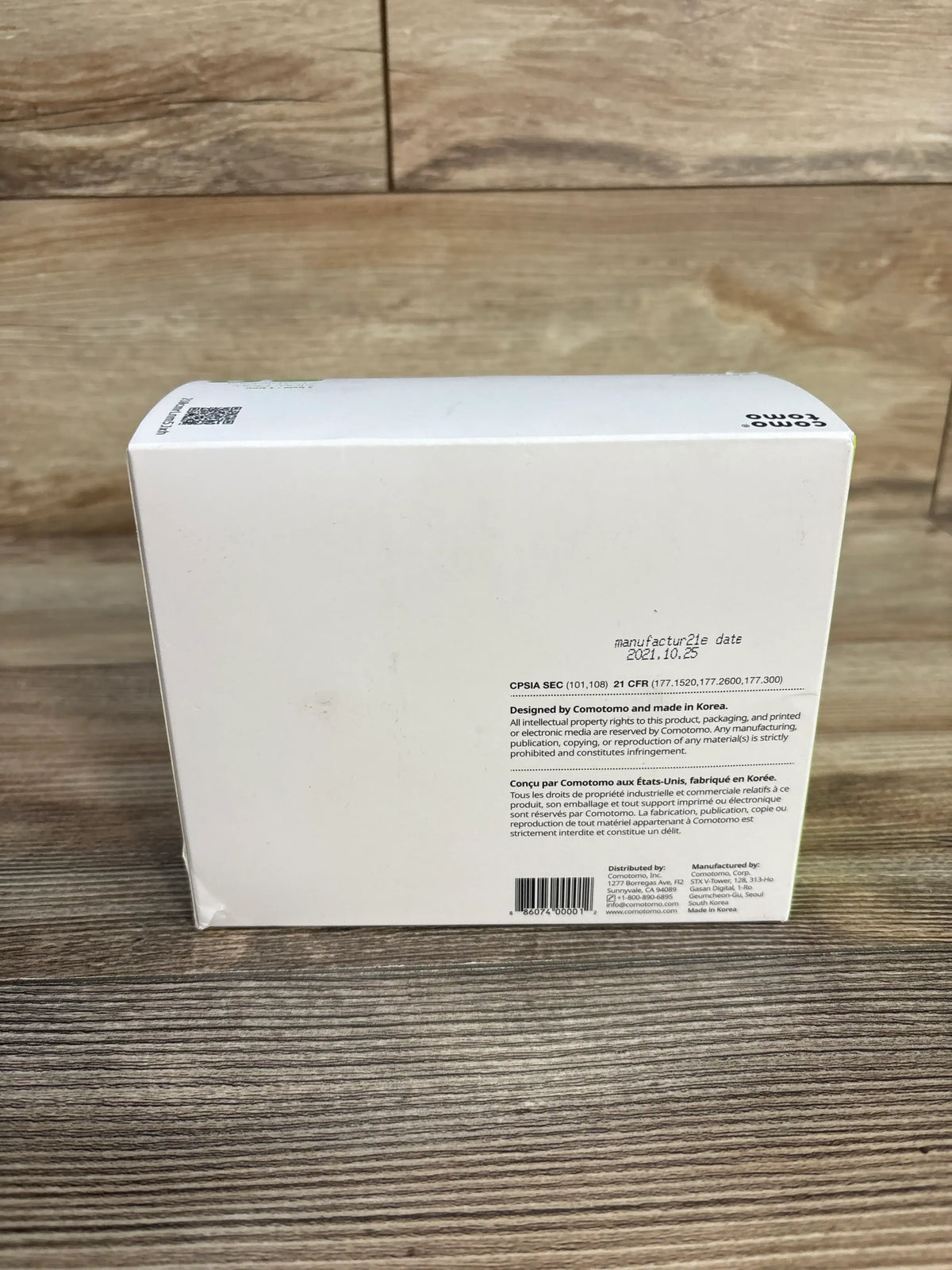 Rear view of the NEW Comotomo 2-pack 5oz baby bottle set packaging with product information on a wood-grain surface