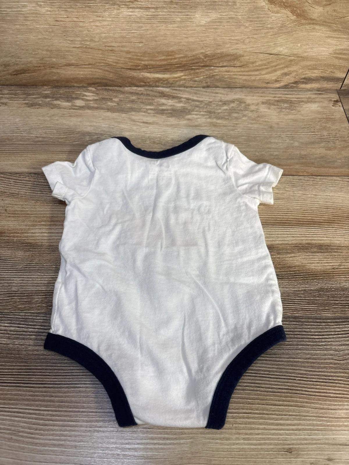 Flat lay back view of white Nike baby bodysuit showing navy trim at neckline and leg openings on wood background