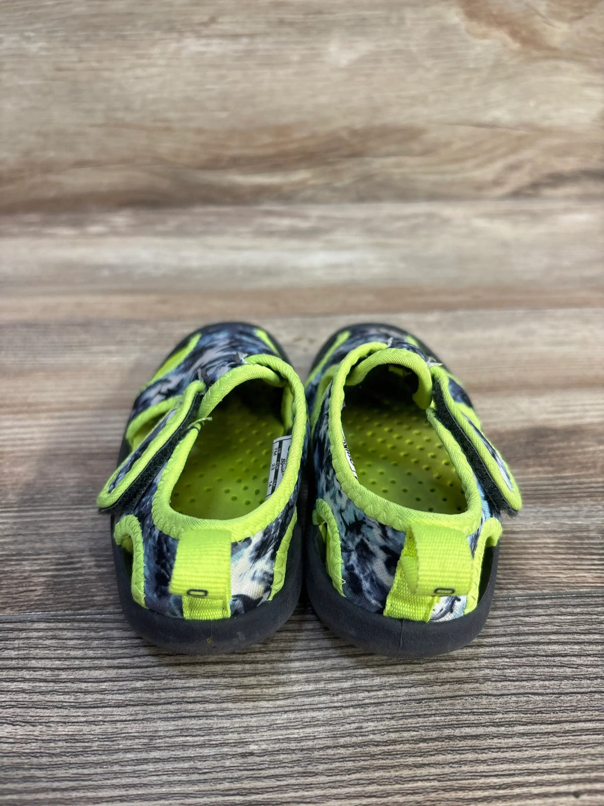 Front view of OshKosh Aquatic Water Shoes showcasing grey and green coloring and hook and loop closures on a wood surface