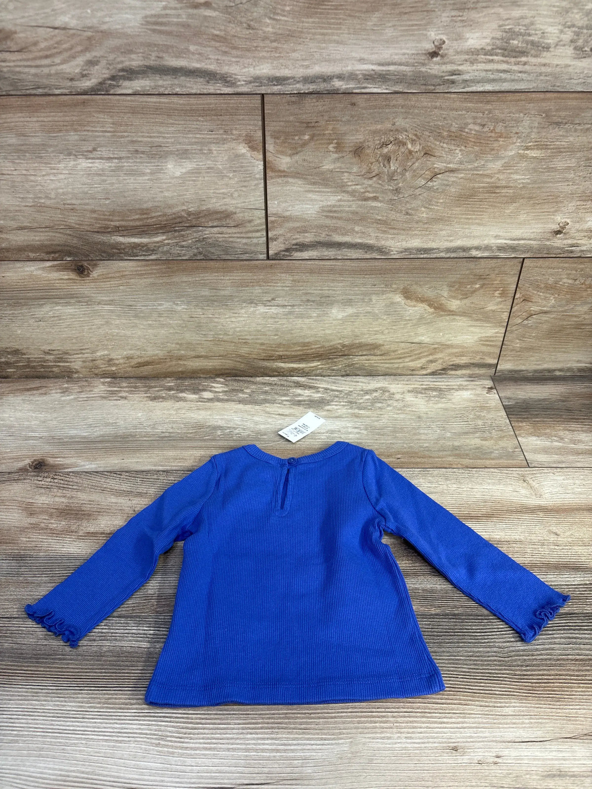 Back view of blue Baby Gap ribbed long sleeve baby shirt showcasing keyhole closure and lettuce trim sleeves on wood grain