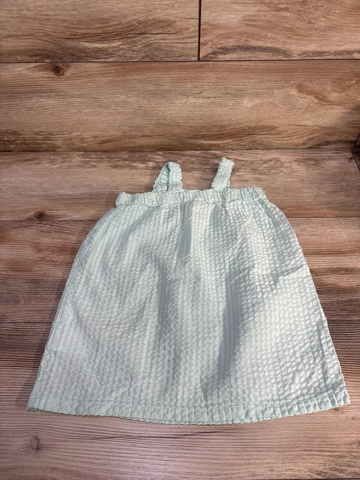 Flat lay of H&M sleeveless mint toddler dress showing textured seersucker fabric and elastic shirred top with thin straps on light wood background
